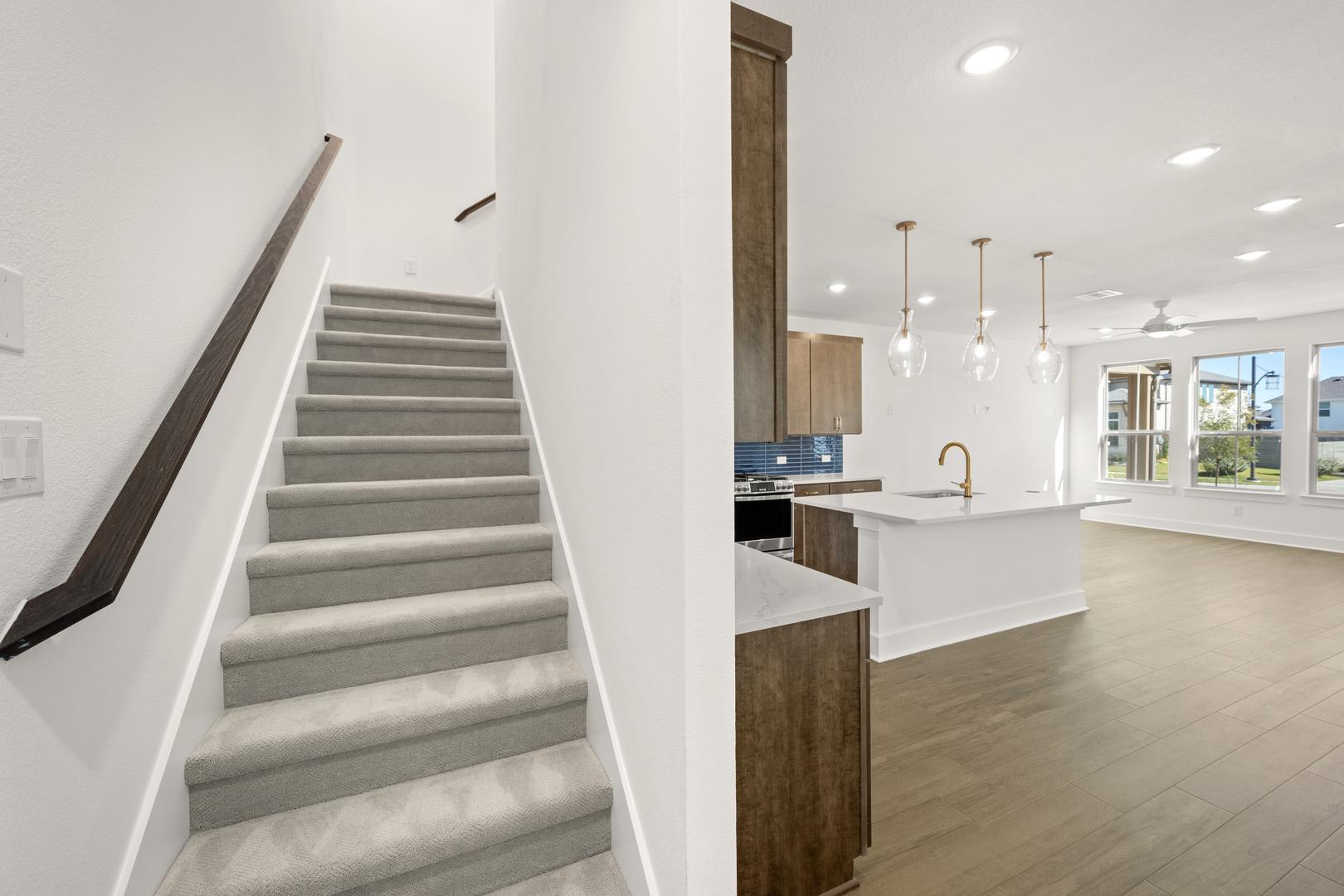 A modern, open-concept interior with a staircase leading to an upper level, a kitchen with white countertops and wooden cabinetry, and a bright, airy atmosphere.