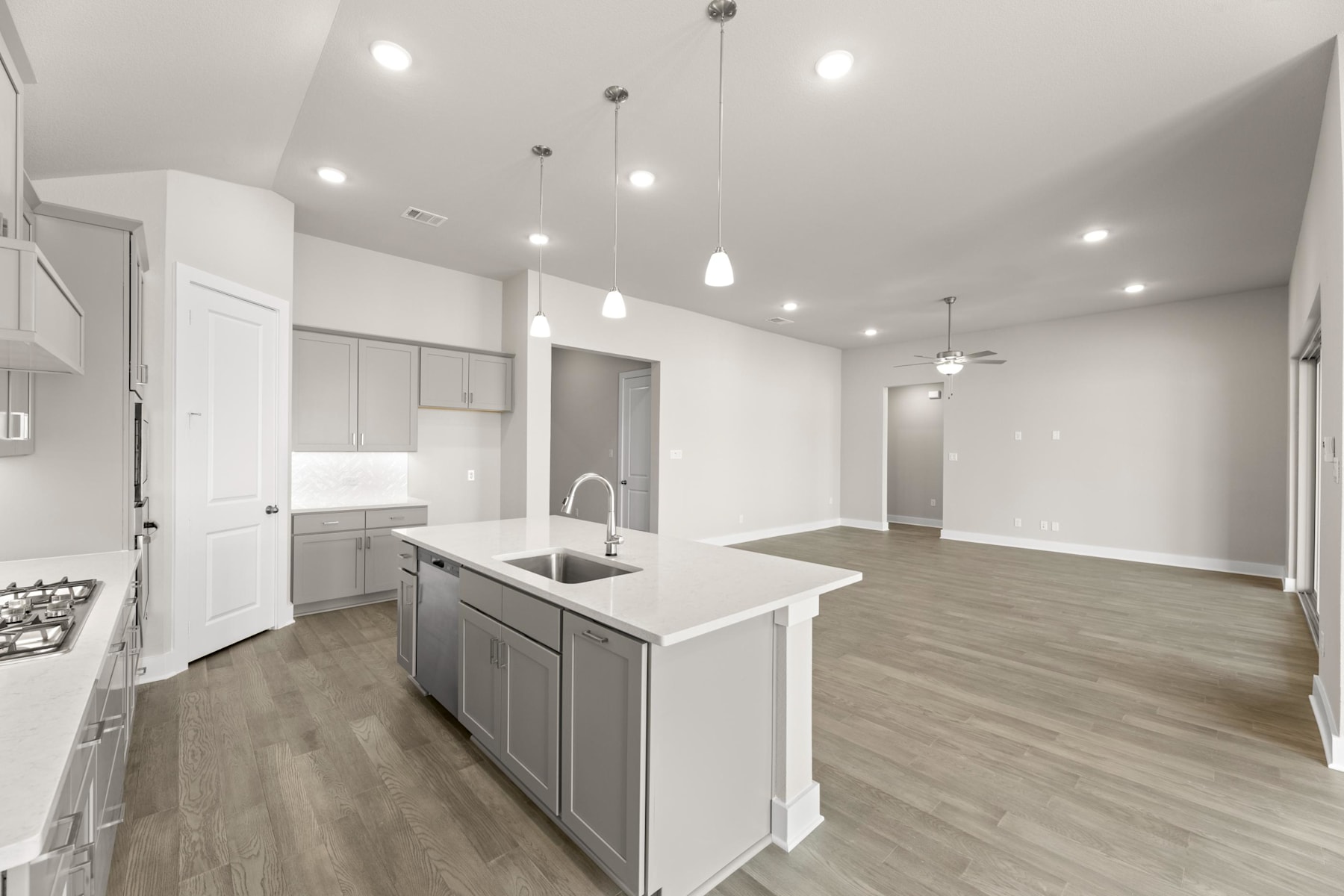 A modern, open-concept kitchen and living space with white walls, gray cabinets, and hardwood flooring.