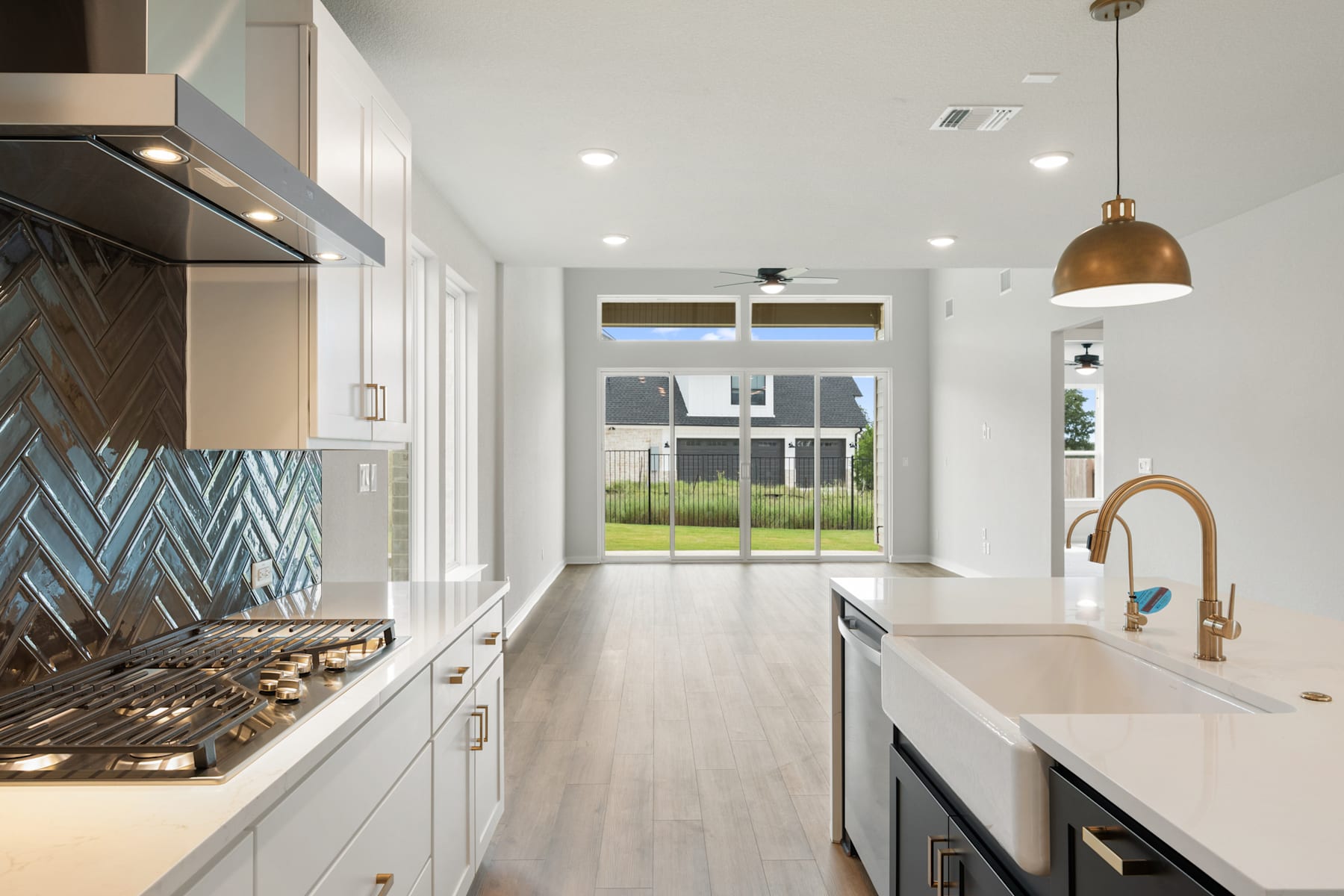 A modern, well-lit kitchen with white cabinets, a patterned tile backsplash, and a large window overlooking a grassy outdoor area.