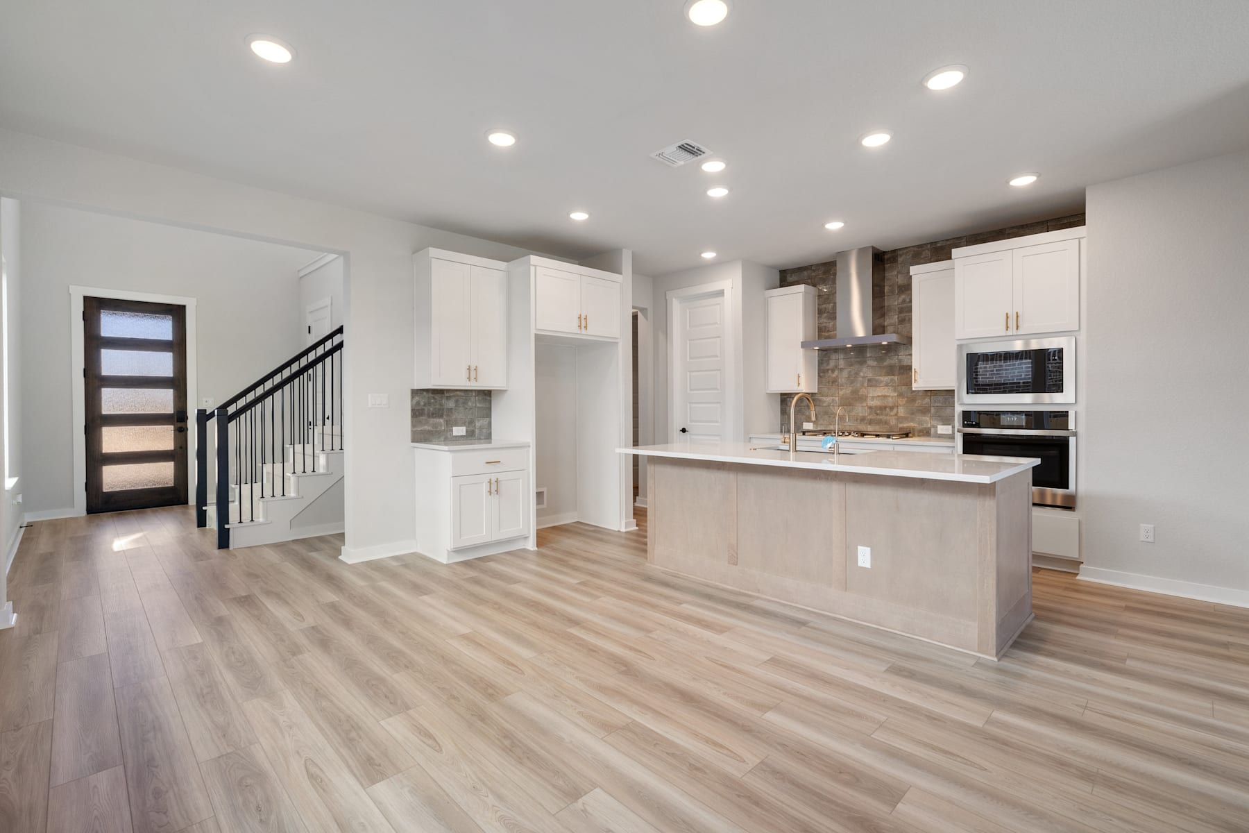 A modern, open-concept kitchen and living space with white cabinets, hardwood floors, and recessed lighting.