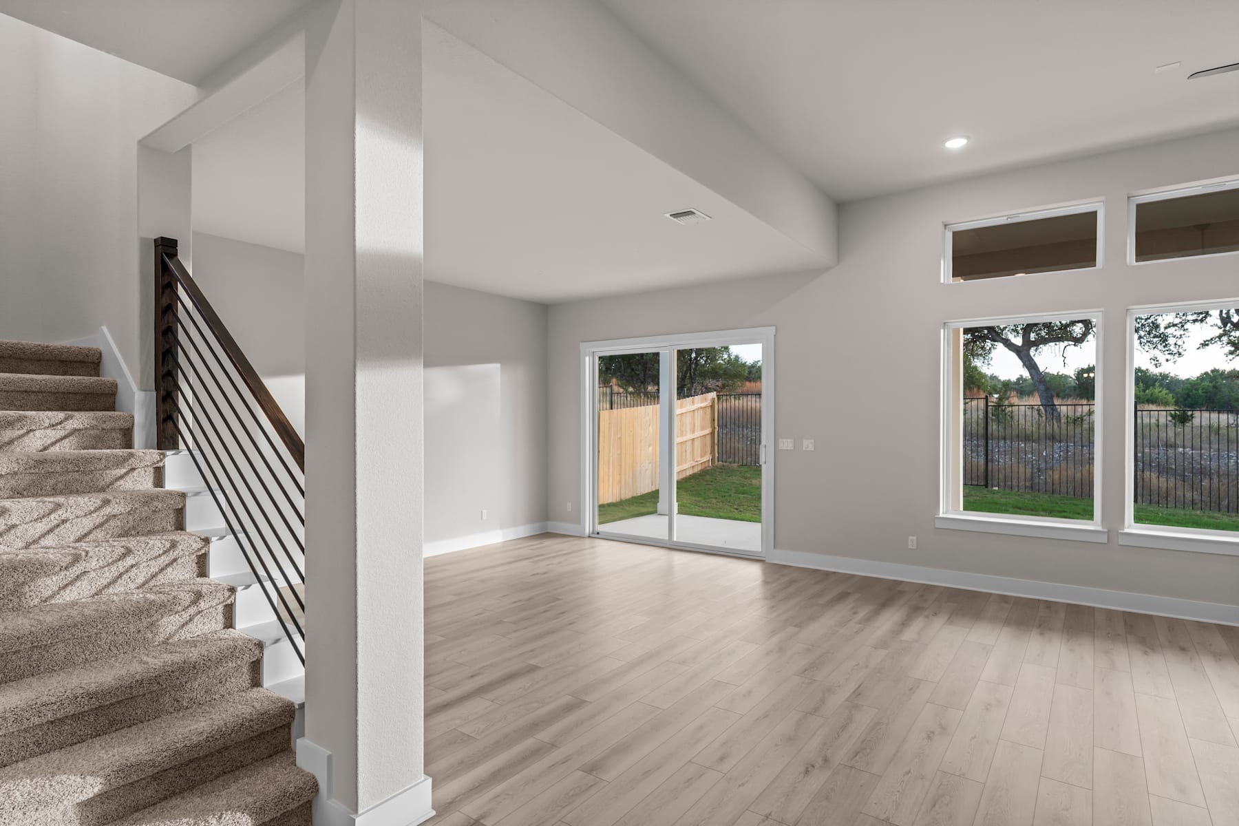 The image shows a spacious and bright interior with a staircase leading up to the second floor, and a sliding glass door that provides a view of the outdoor area.