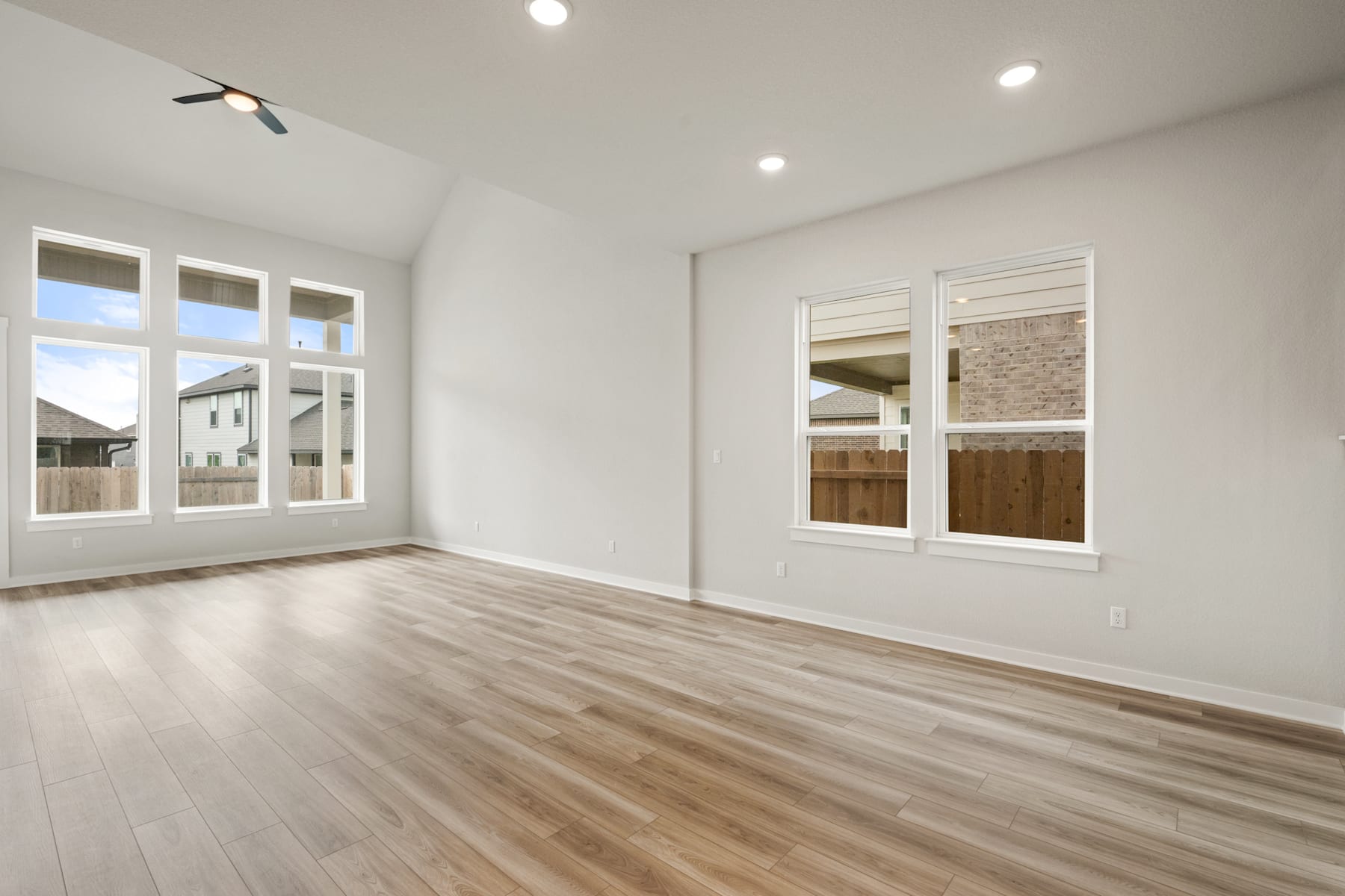 A spacious, well-lit room with hardwood floors, white walls, and large windows providing natural light.