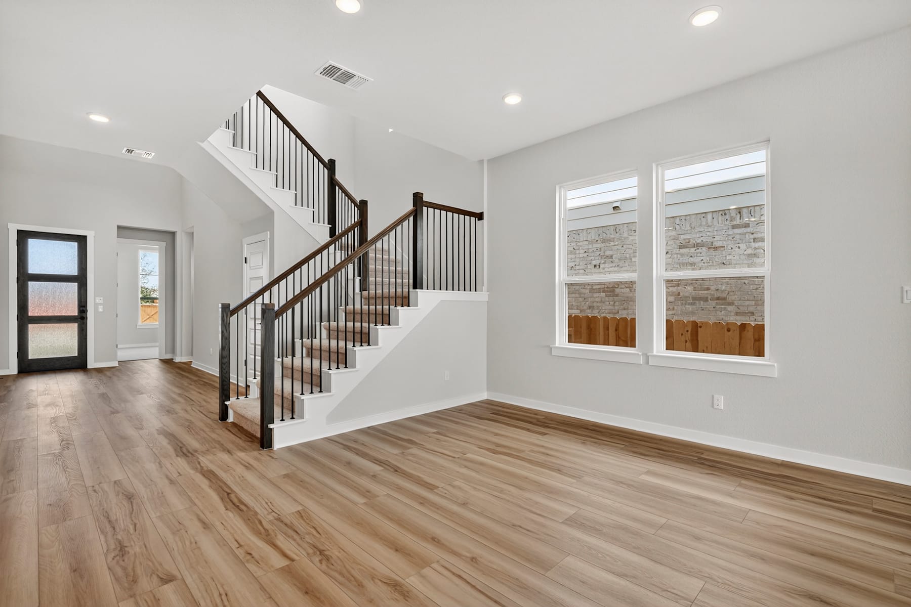 A spacious and well-lit interior with a wooden staircase, hardwood floors, and large windows providing natural light.