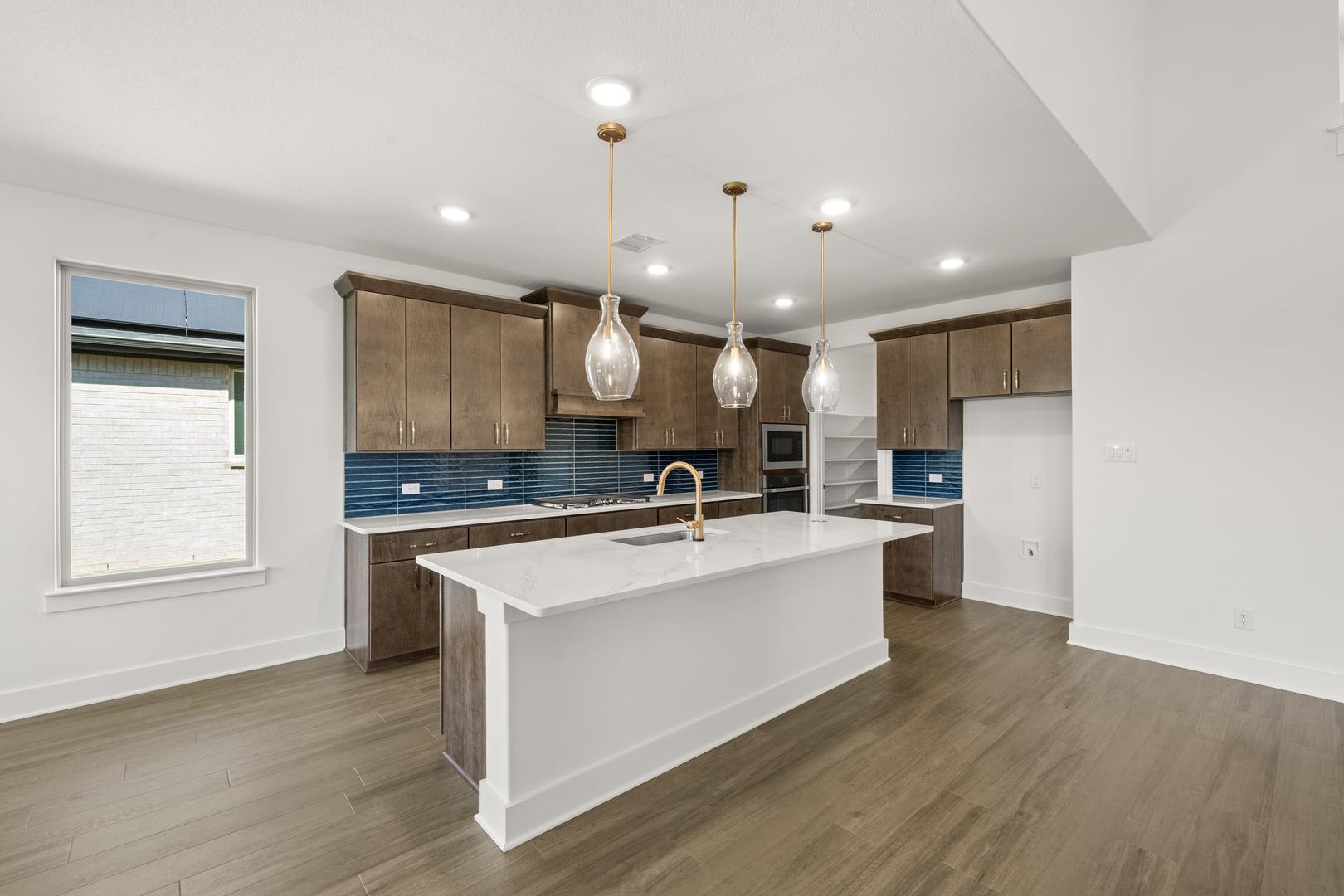 A modern and spacious kitchen with a white island, wooden cabinets, and pendant lighting fixtures, set against a backdrop of hardwood floors and a bright, airy atmosphere.