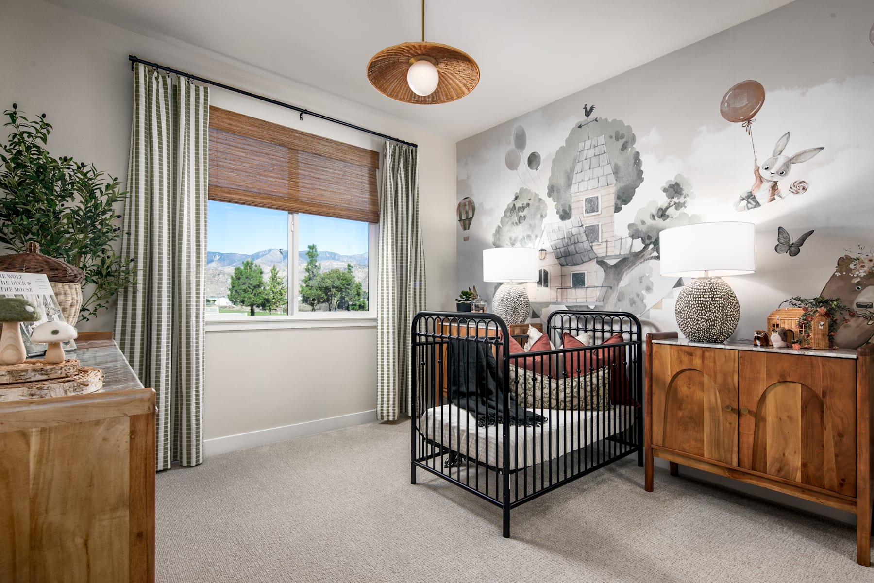 A cozy and well-decorated nursery with a metal crib, wooden furniture, and a nature-inspired wall mural, surrounded by lush greenery visible through the window.