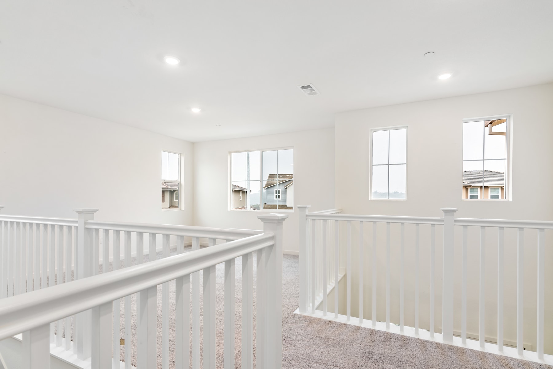 A bright and airy interior with a white staircase railing leading up to a second floor, surrounded by large windows letting in natural light.