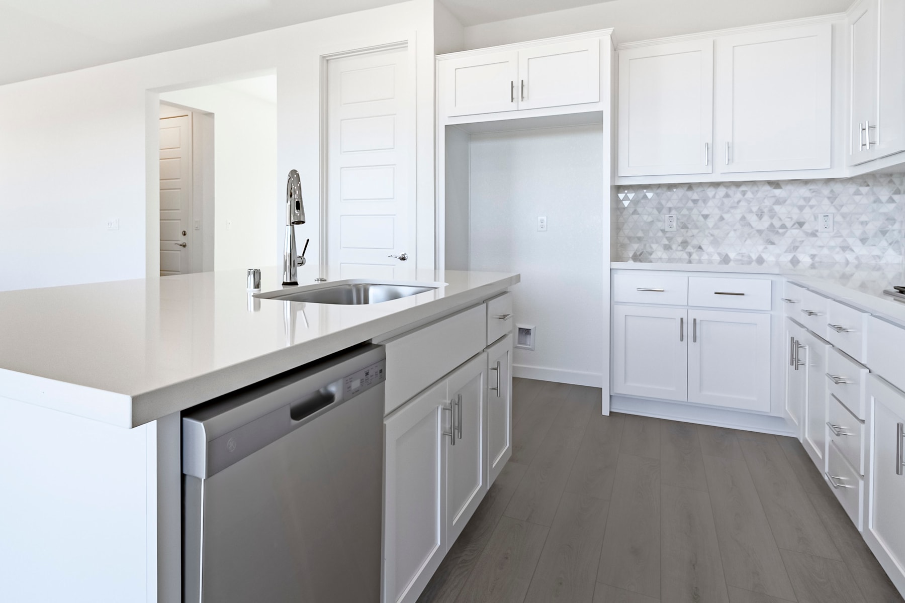 A modern, bright kitchen with white cabinets, a stainless steel dishwasher, and a gray tile backsplash.