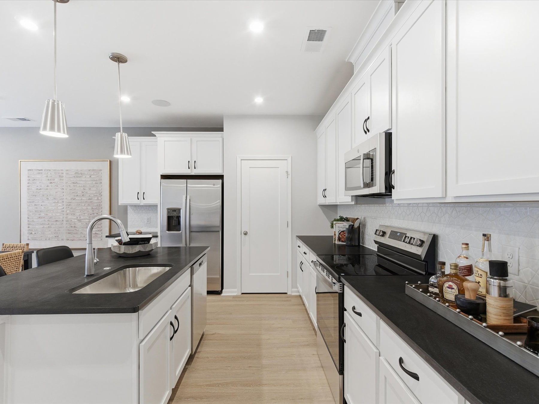 A modern, well-lit kitchen with white cabinets, black countertops, and stainless steel appliances, creating a sleek and stylish atmosphere.