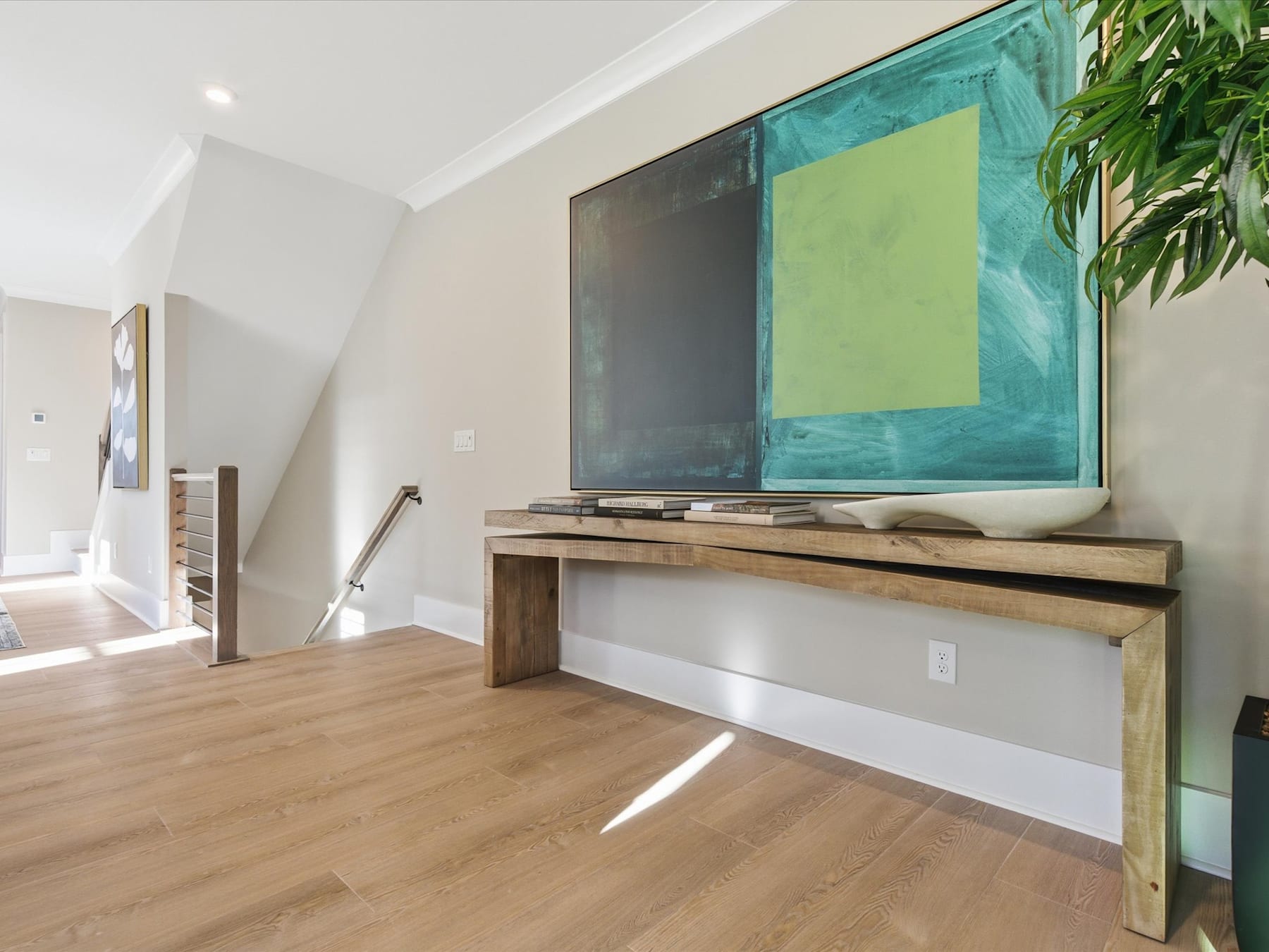 A modern living room with a large abstract painting on the wall, a wooden console table, and a potted plant in the background.