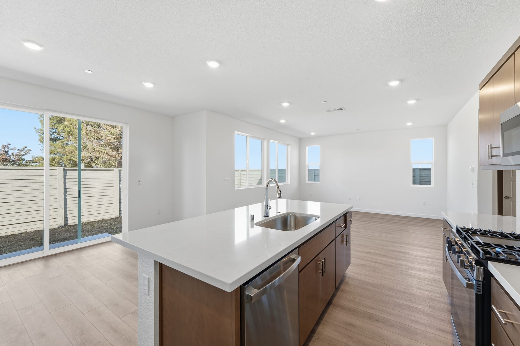 A modern, open-concept kitchen with white countertops, wooden cabinets, and large windows overlooking a scenic outdoor area.