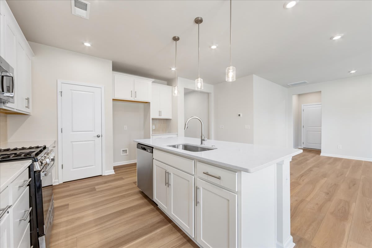 A modern, open-concept kitchen with white cabinets, a large island, and hardwood floors, illuminated by pendant lights.