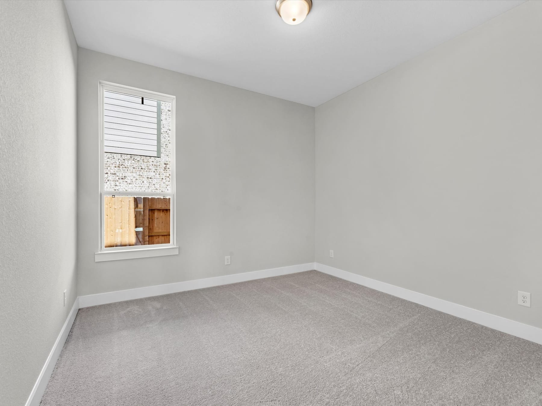 A sparsely furnished room with a window, a light fixture, and a gray carpeted floor.