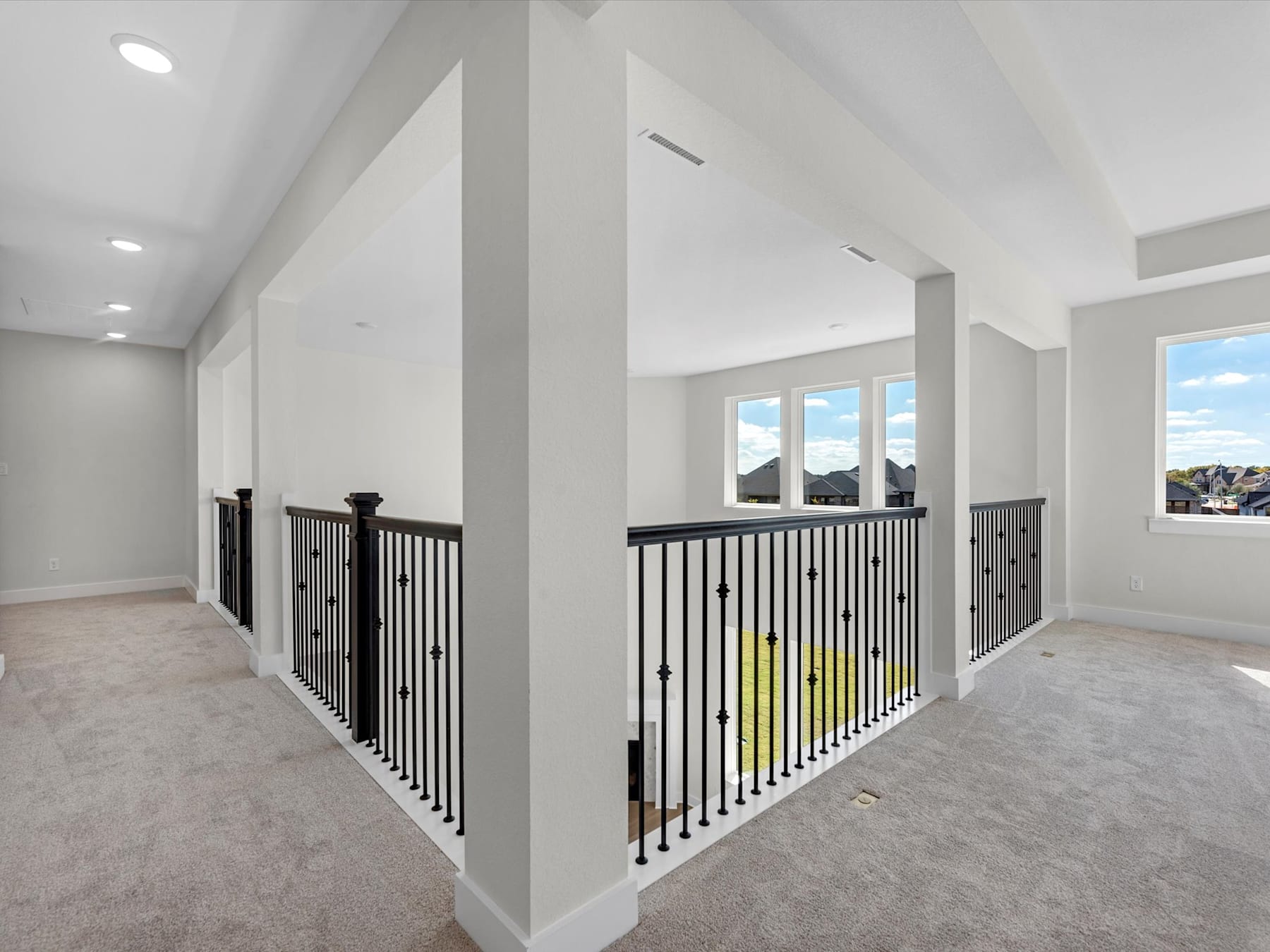 A spacious, open-concept interior with a second-floor balcony overlooking the room, featuring white walls, gray carpeting, and a black metal railing.
