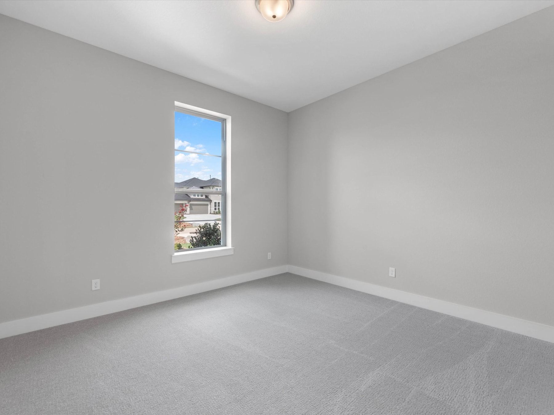 A bright, empty room with a window overlooking a residential neighborhood in the background.