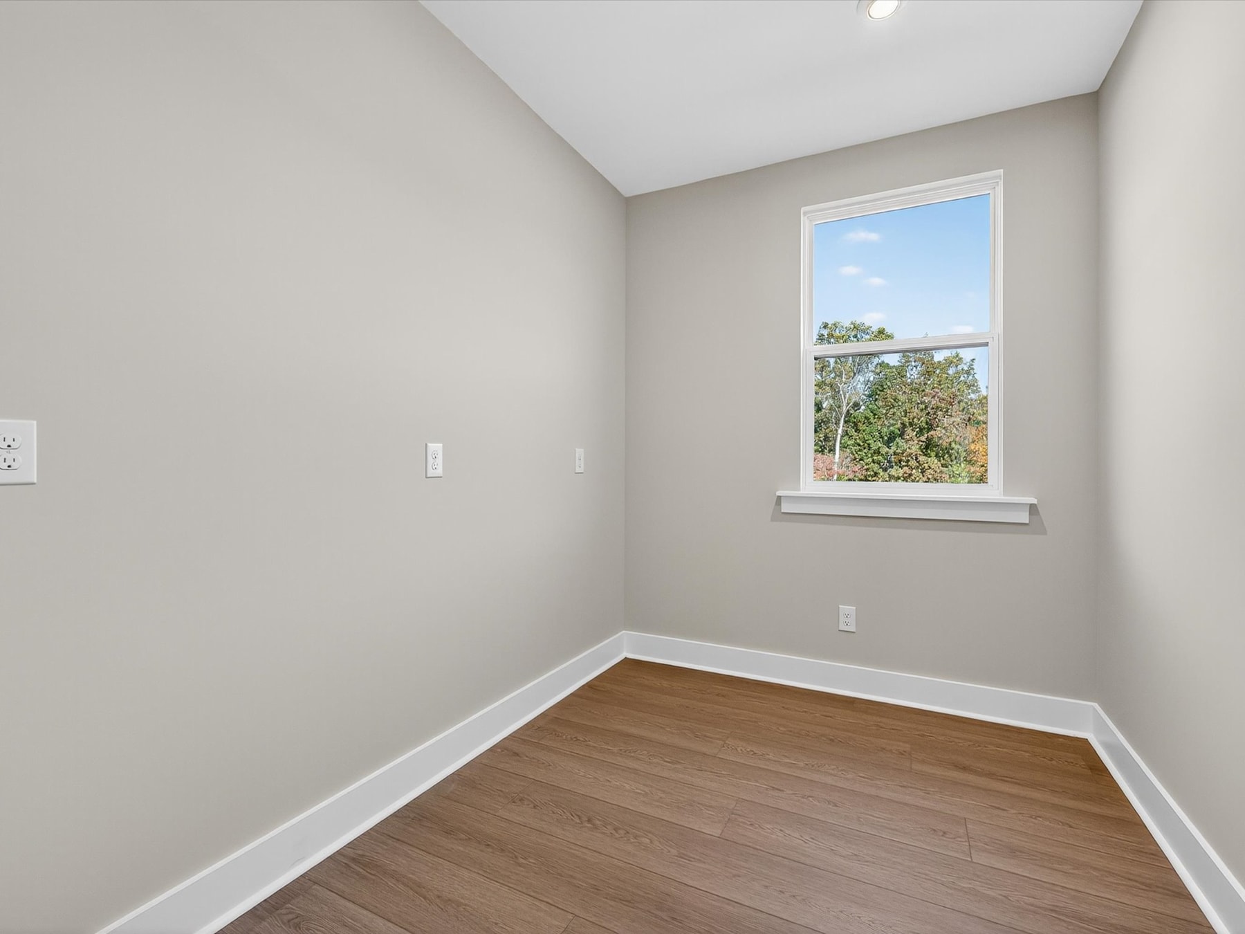 A spacious, well-lit room with a large window overlooking a scenic outdoor view, featuring a hardwood floor and neutral-colored walls.