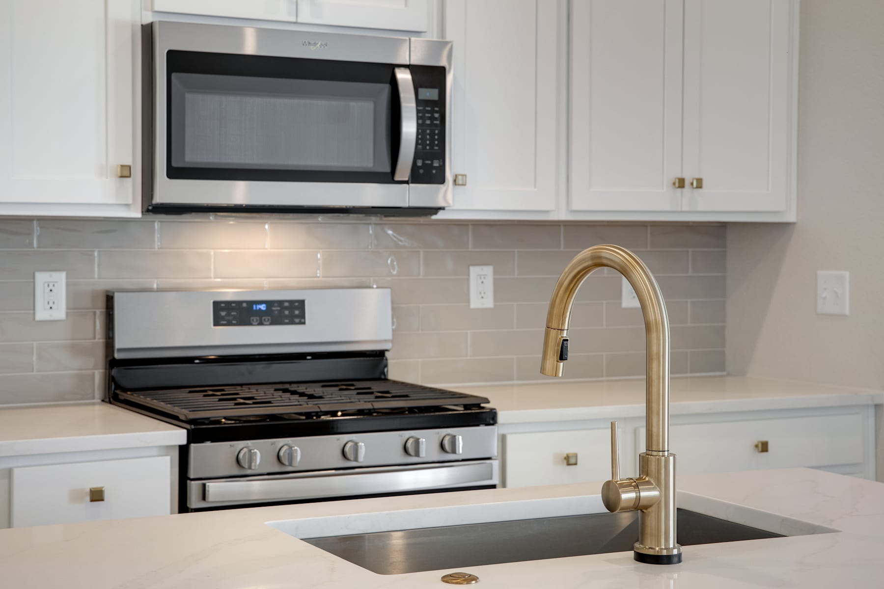 A modern kitchen with white cabinets, a stainless steel oven, and a gold-colored faucet over a stainless steel sink.