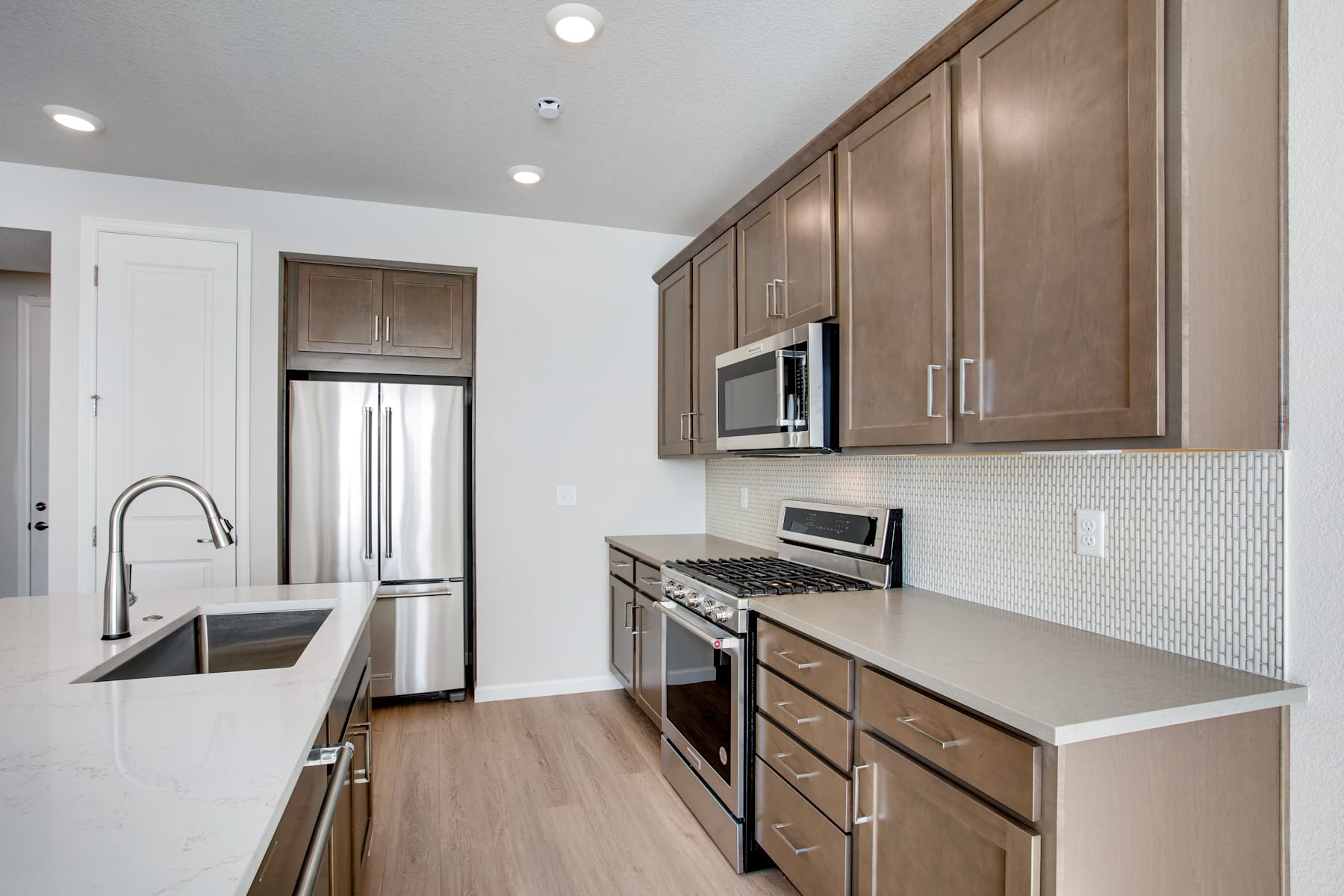 A modern, well-equipped kitchen with stainless steel appliances, wooden cabinets, and a tiled backsplash, set against a light-colored hardwood floor.