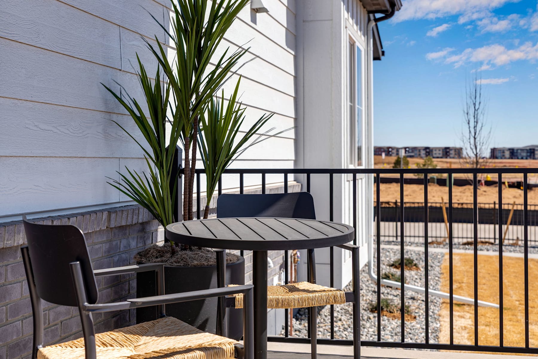 A cozy balcony with a round table, chairs, and potted plants overlooking a snowy cityscape in the background.