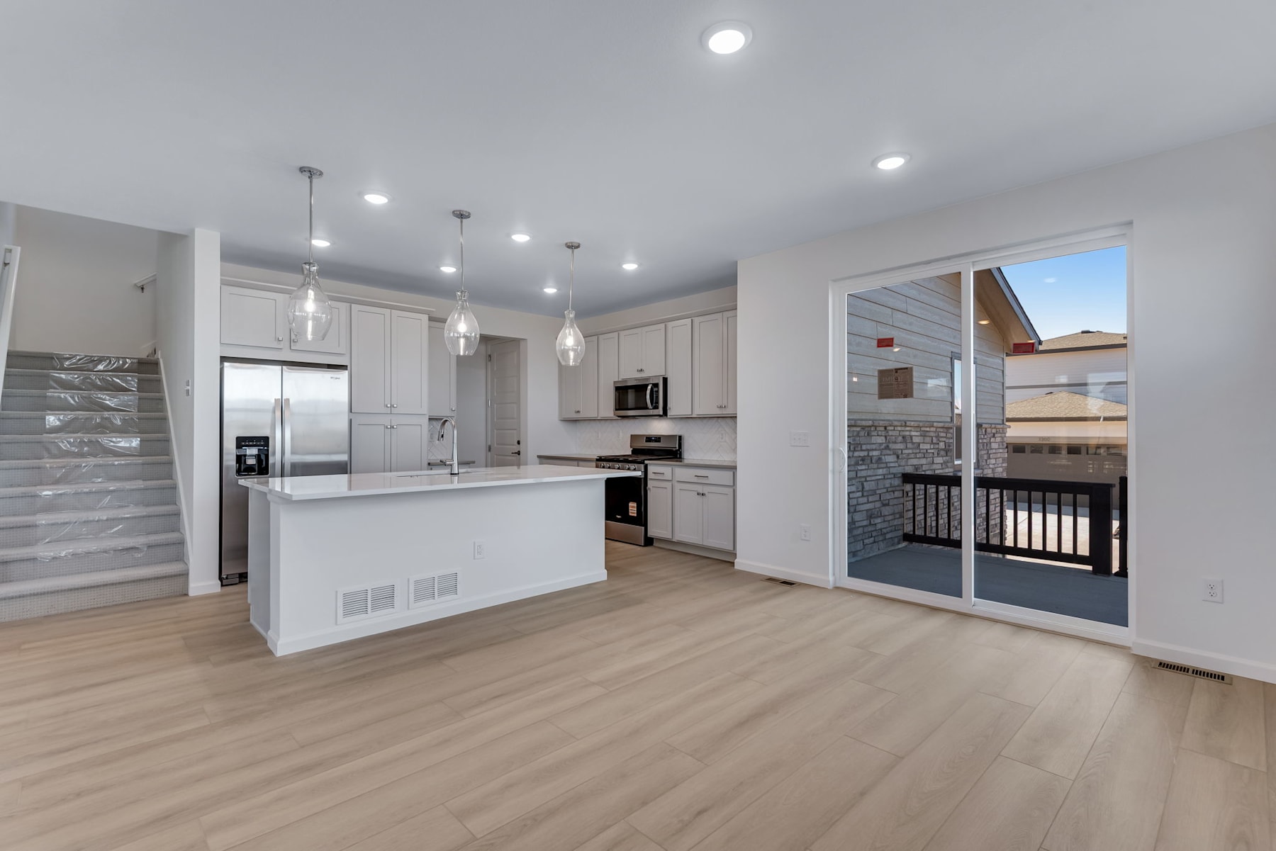 A modern, open-concept kitchen with white cabinets, stainless steel appliances, and a sliding glass door leading to a balcony or patio area.