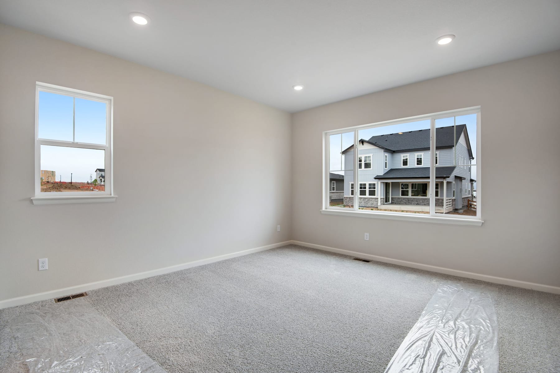 A spacious, well-lit room with large windows overlooking a residential neighborhood in the background.