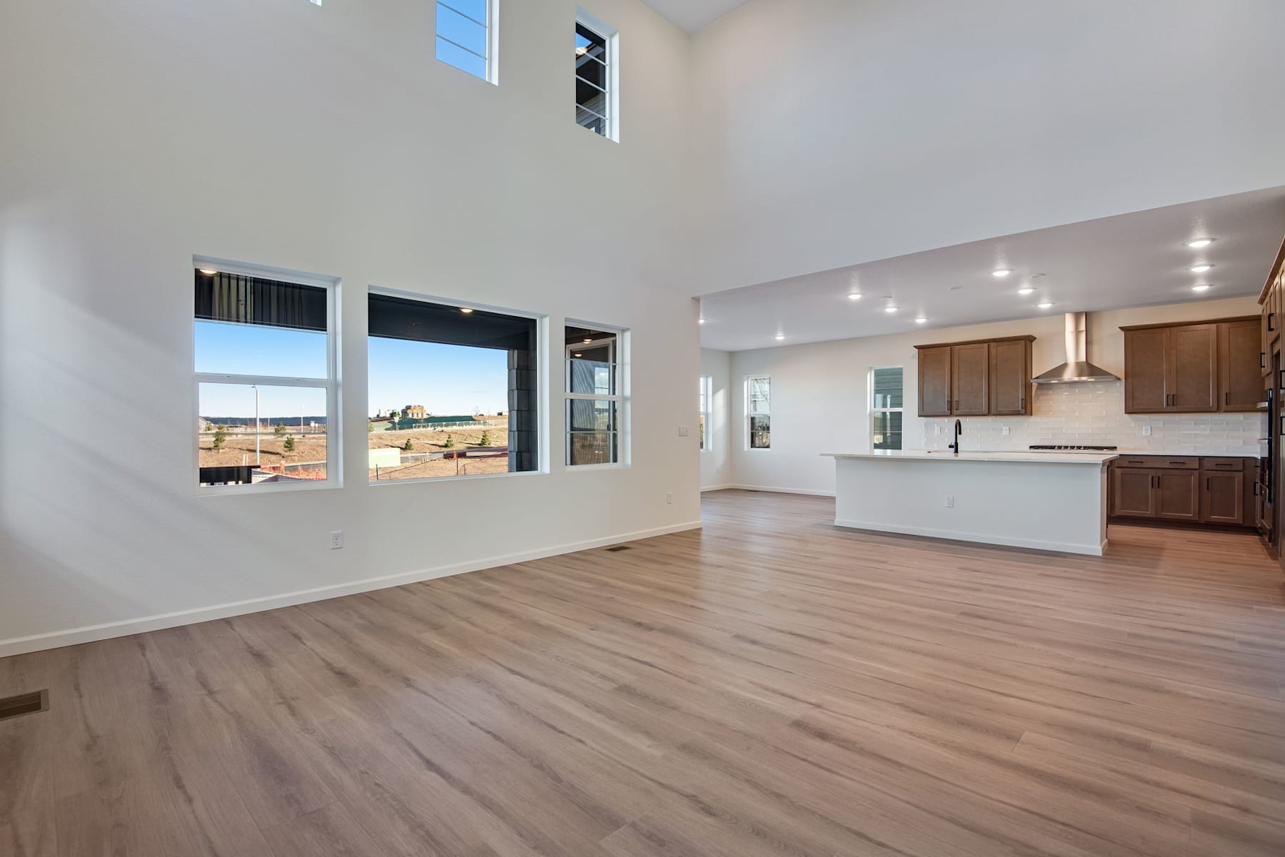 A spacious and bright open-concept living area with a kitchen, hardwood floors, and large windows offering a scenic view of the outdoors.