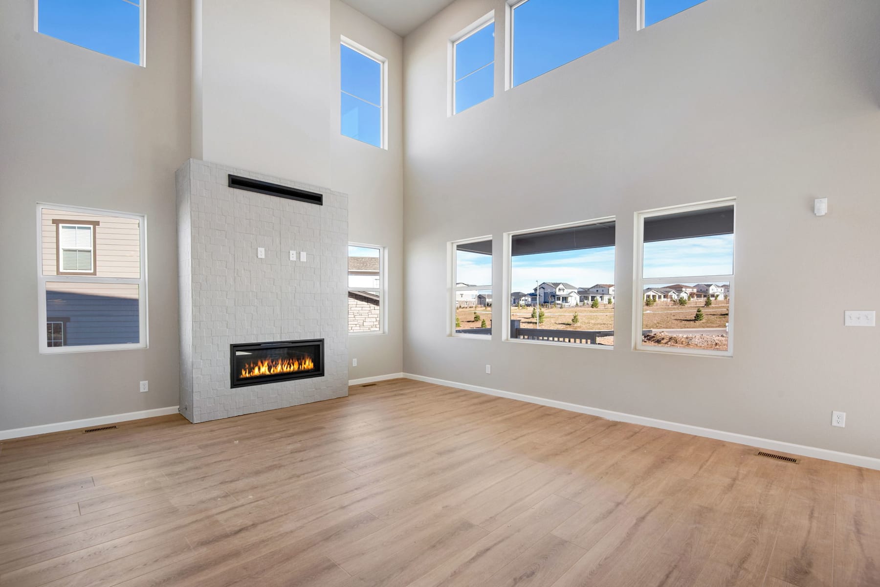 A spacious and bright living room with a fireplace, large windows, and hardwood floors, overlooking a scenic outdoor landscape.