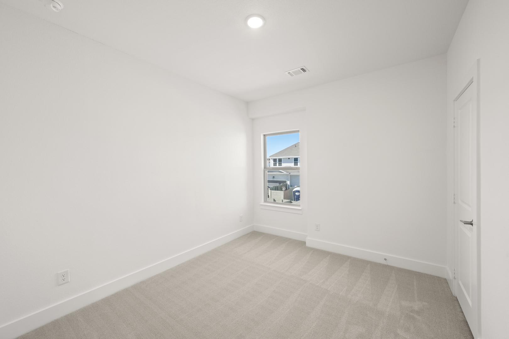 A bright, empty room with white walls and a wooden floor, featuring a window that provides natural light.