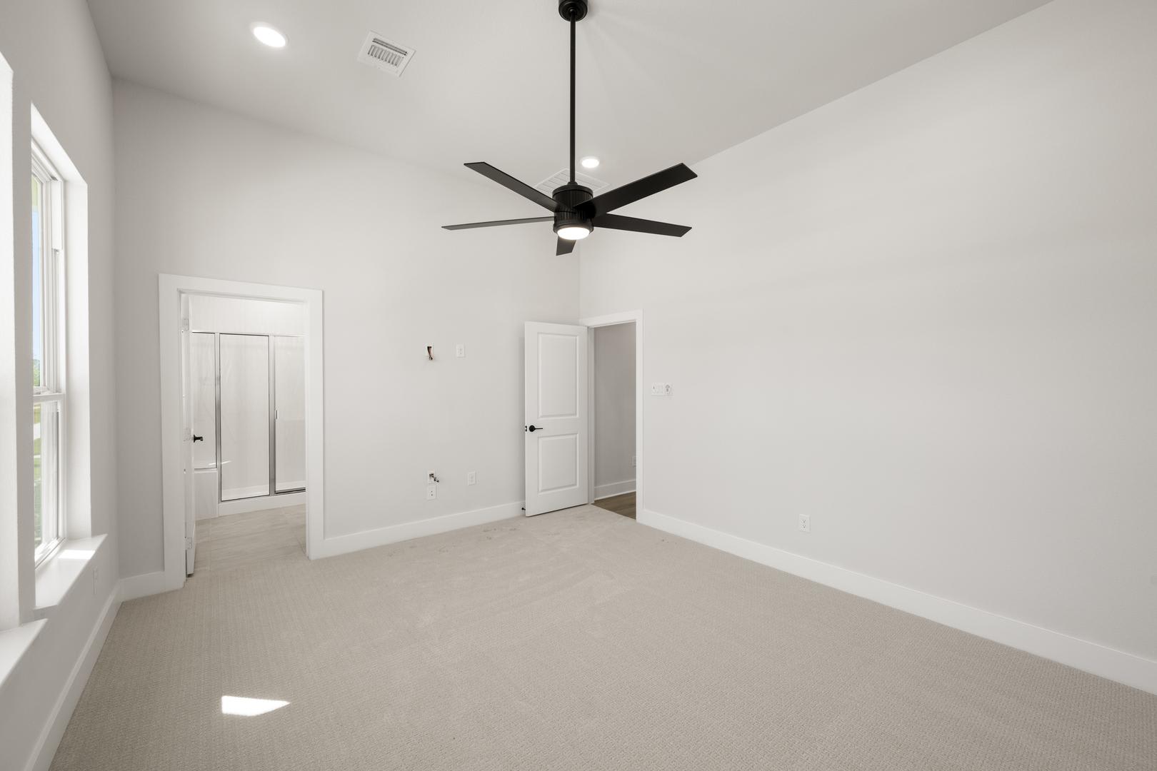A spacious, minimalist room with a ceiling fan and two doors, featuring a clean, white interior and hardwood flooring.