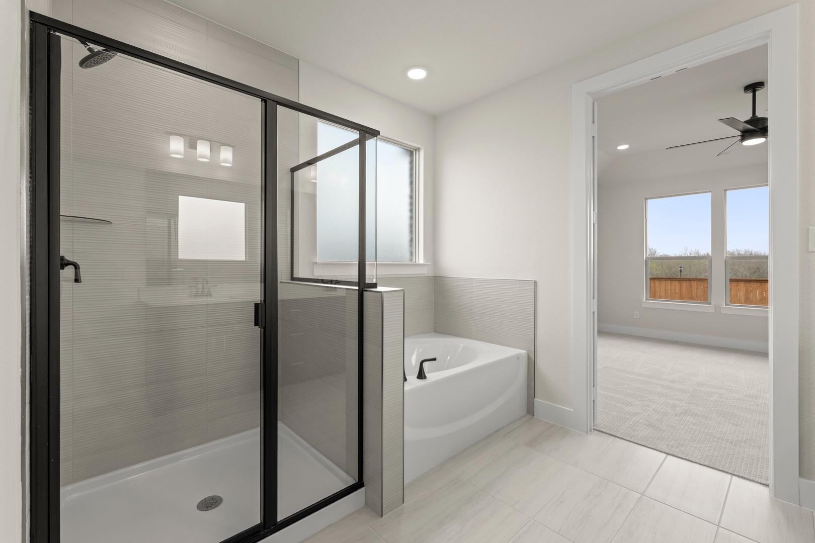 A modern, minimalist bathroom with a glass-enclosed shower, a freestanding bathtub, and large windows providing natural light.