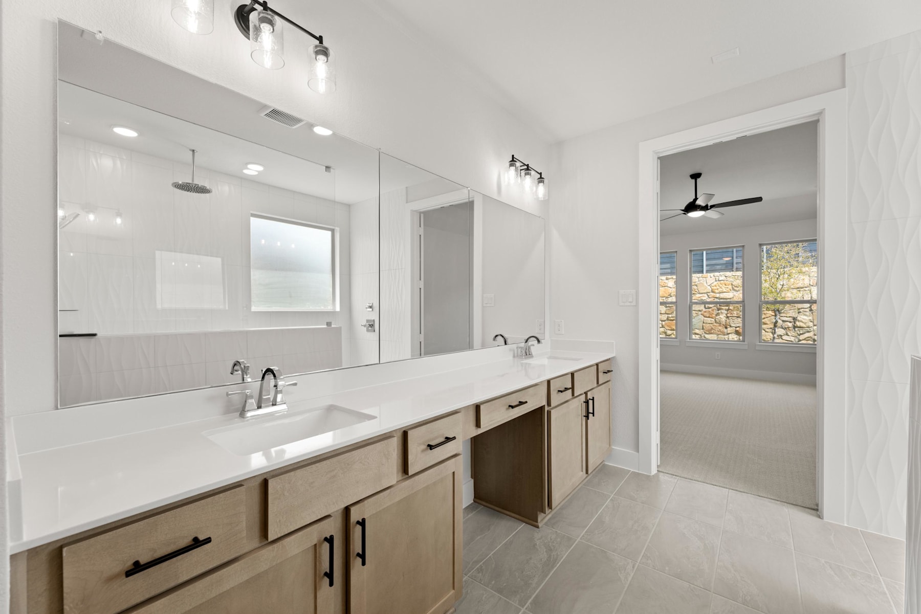 A modern and spacious bathroom with a large vanity, double sinks, and a window providing natural light.