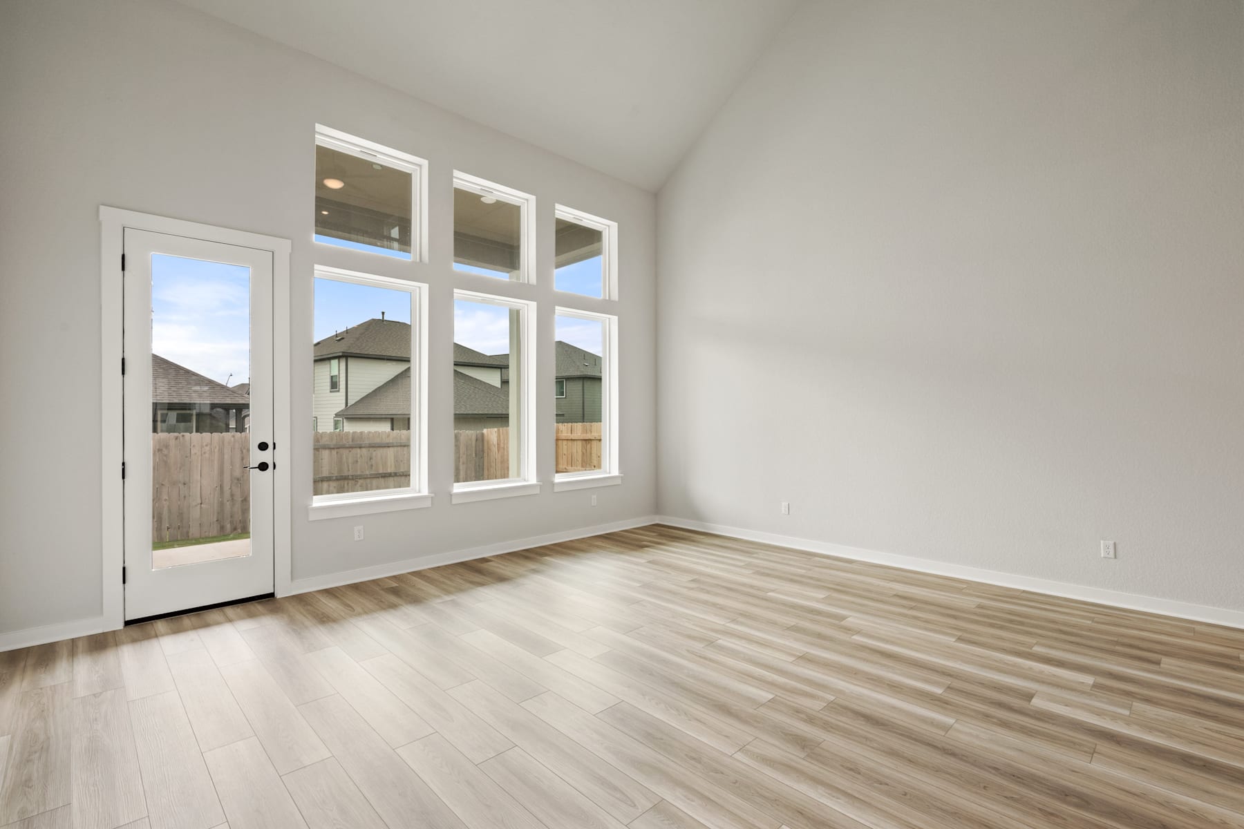 A bright and spacious room with a wooden floor, white walls, and a glass door leading to the exterior of the building.