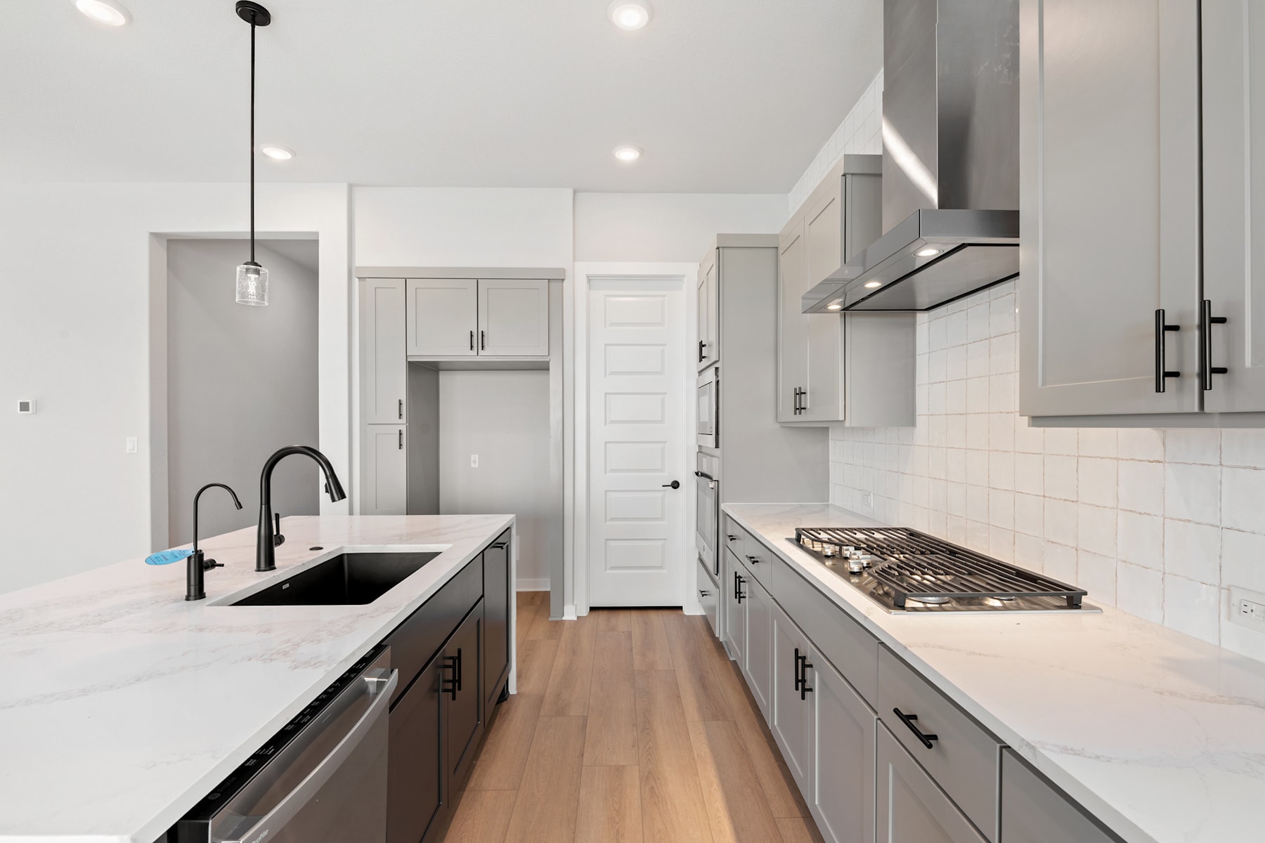 A modern, minimalist kitchen with white cabinets, a marble countertop, and a gas stove in the foreground, leading to a hallway in the background.