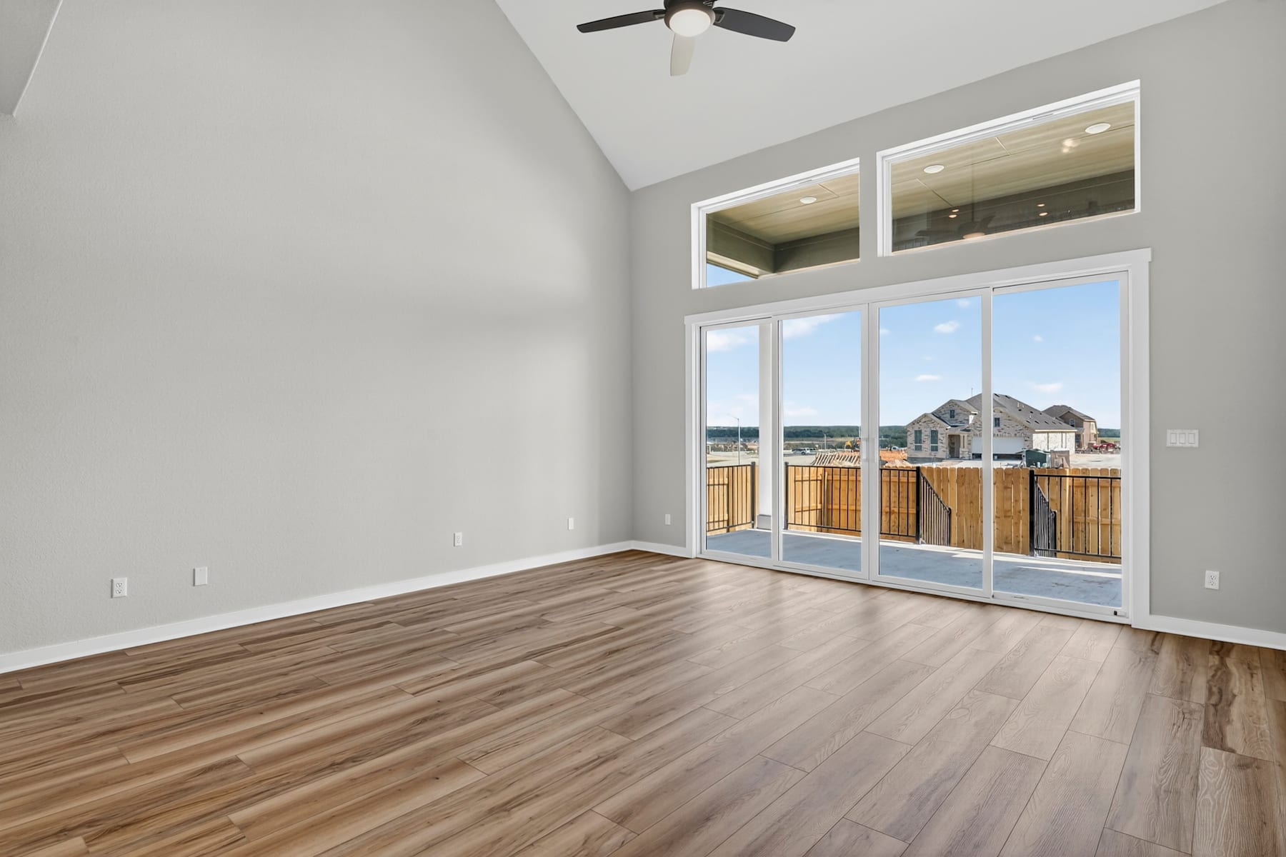 A spacious and bright room with large windows overlooking a scenic outdoor area, featuring hardwood floors and a ceiling fan.