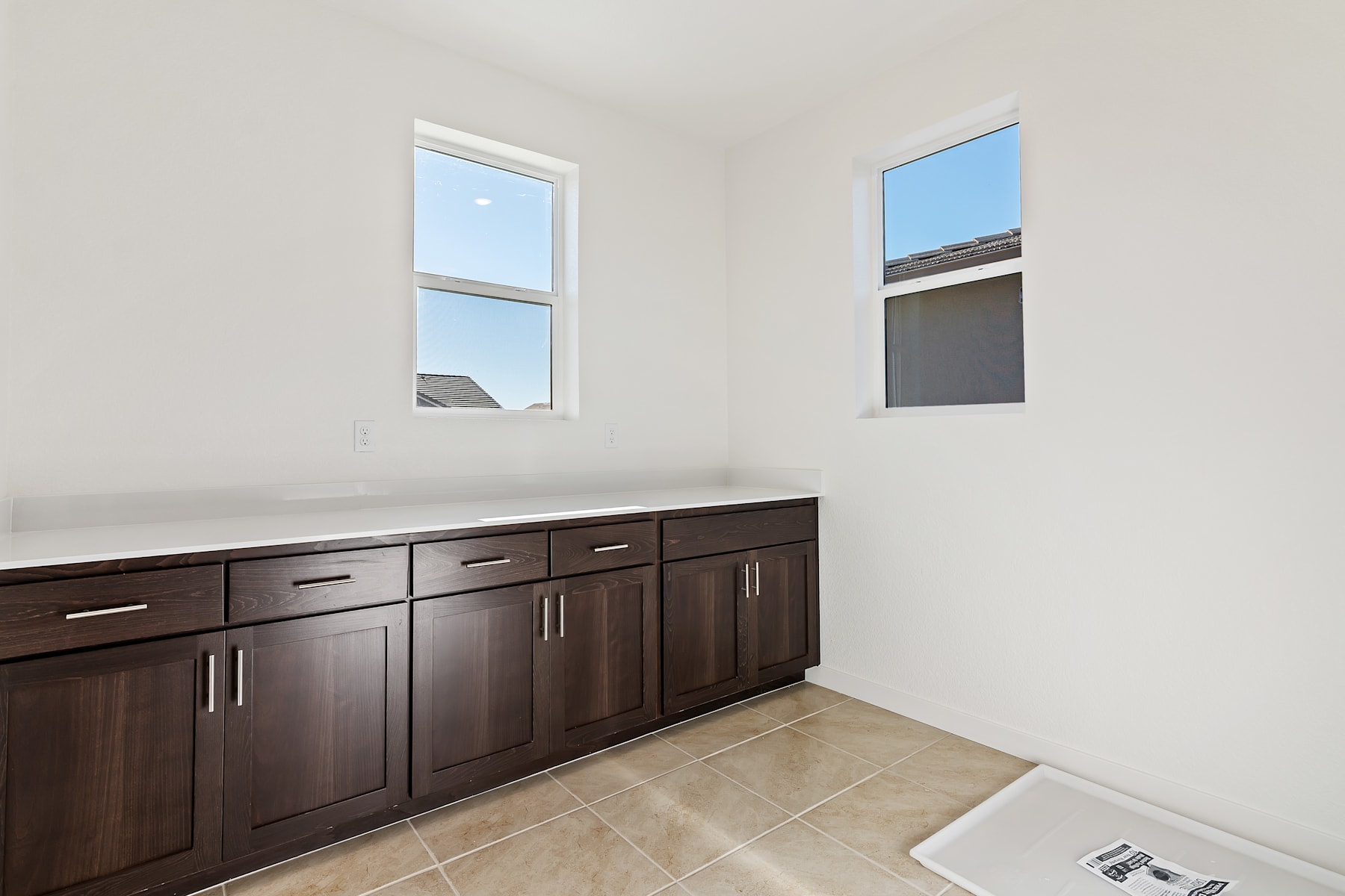 A spacious room with dark wooden cabinets and tiled flooring, illuminated by natural light from the windows.