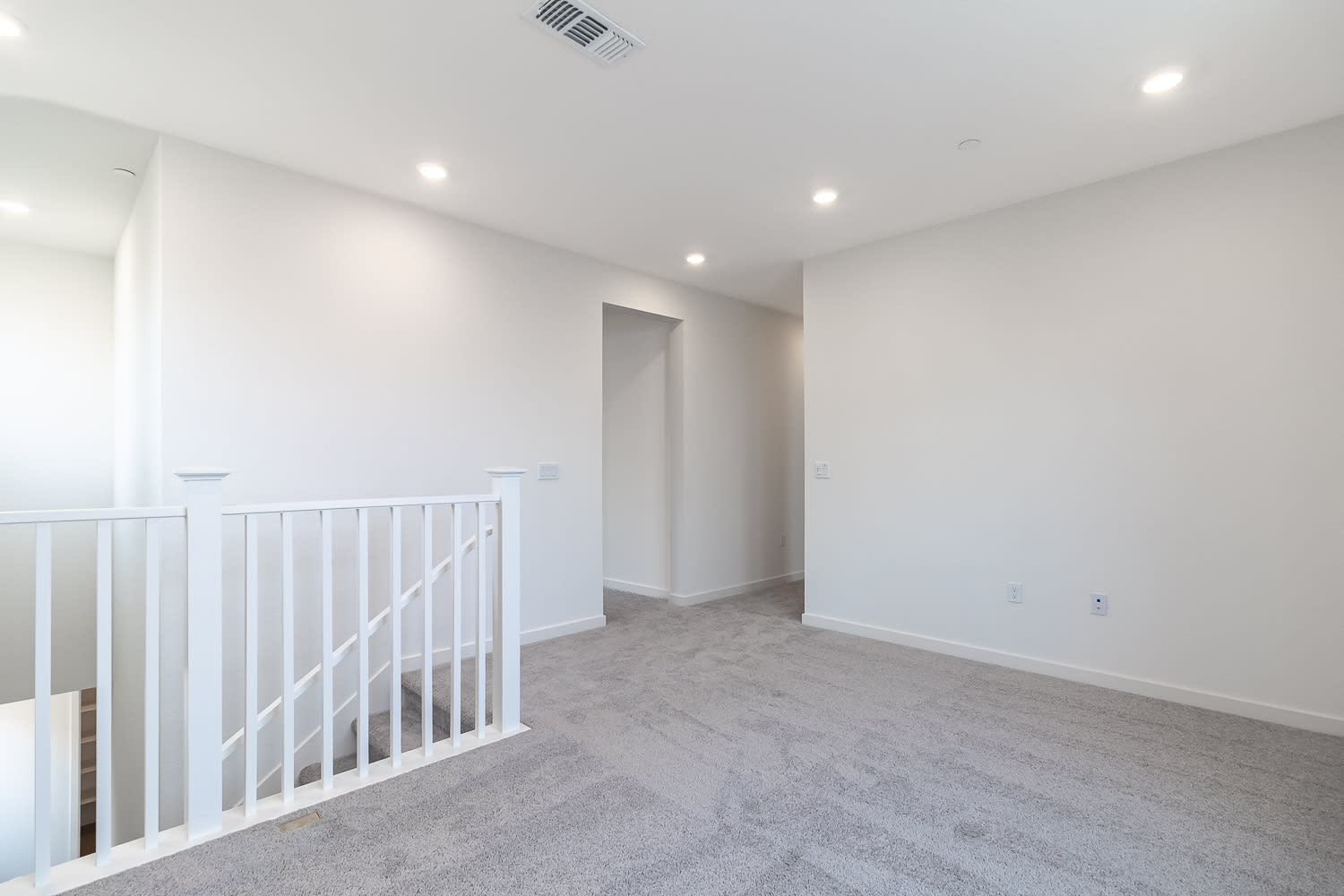 A bright, open-concept room with a white railing and a hallway leading to another area.