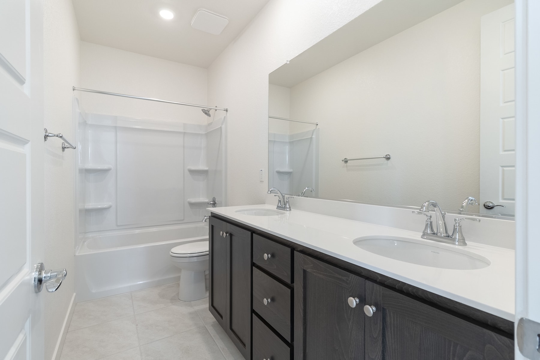 A modern and well-lit bathroom with a dark vanity cabinet, a white countertop, and a large mirror on the wall.