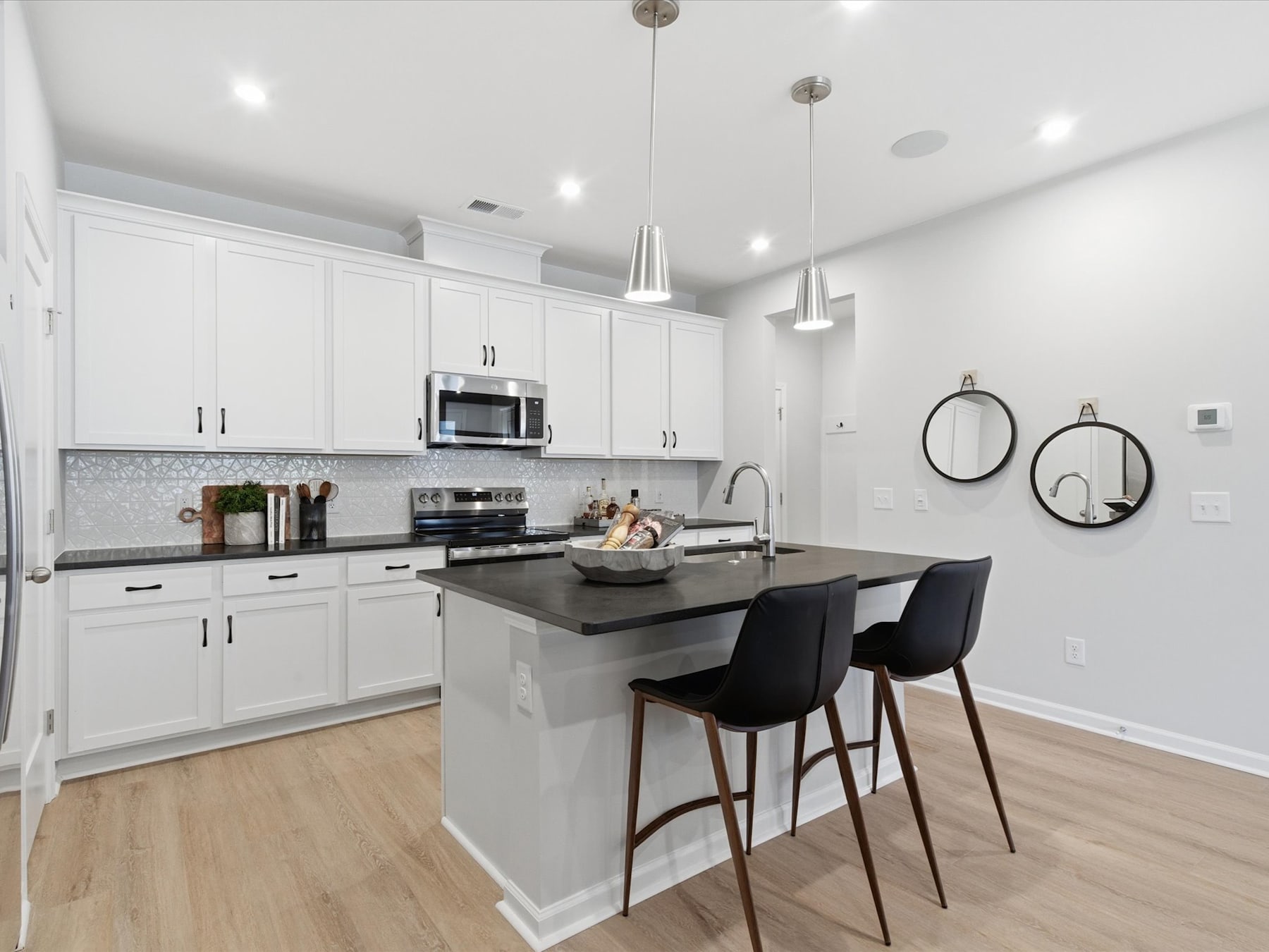 A modern, well-lit kitchen with white cabinets, a gray countertop, and pendant lights hanging above a breakfast bar with black stools.
