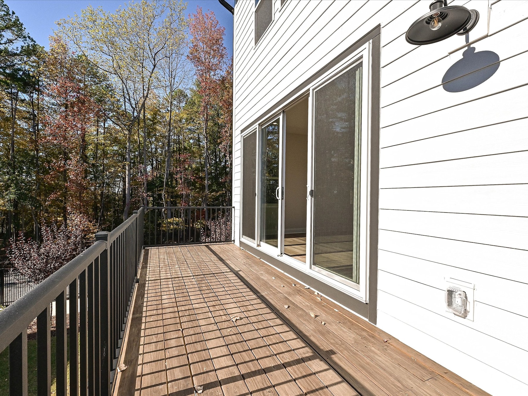 A wooden deck extends from a modern house, surrounded by a lush forest landscape with trees in various stages of autumn foliage.