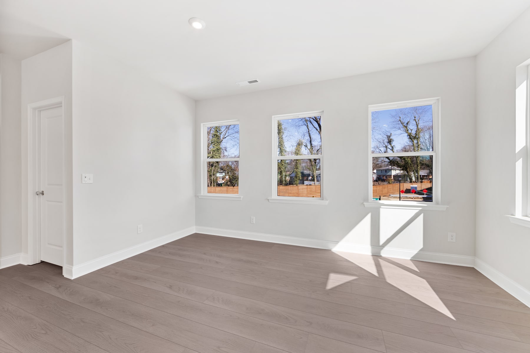 A bright and airy room with large windows overlooking a scenic outdoor landscape, featuring hardwood floors and a minimalist interior design.