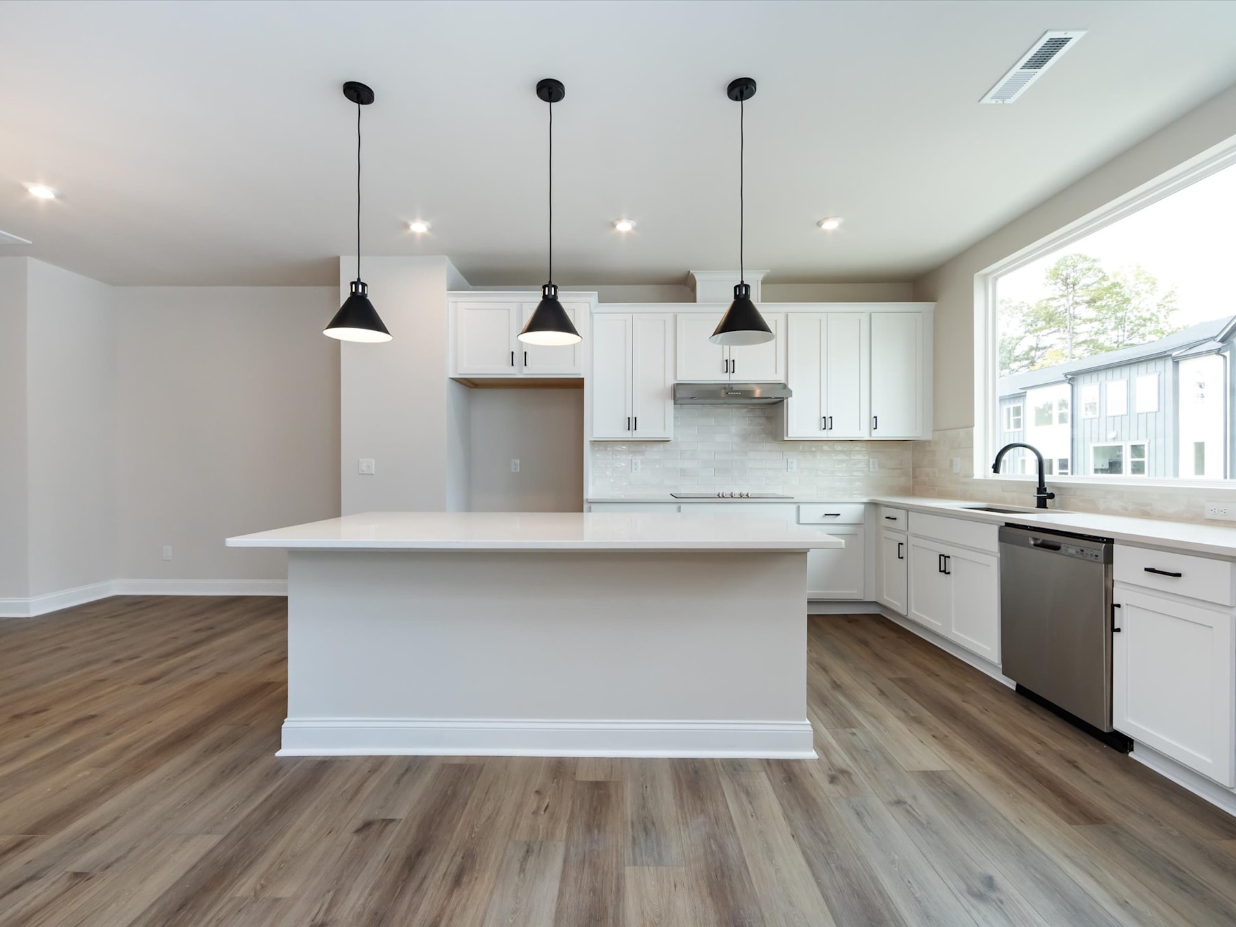 A modern, bright kitchen with white cabinets, a marble-like countertop, and a central island with pendant lighting fixtures.