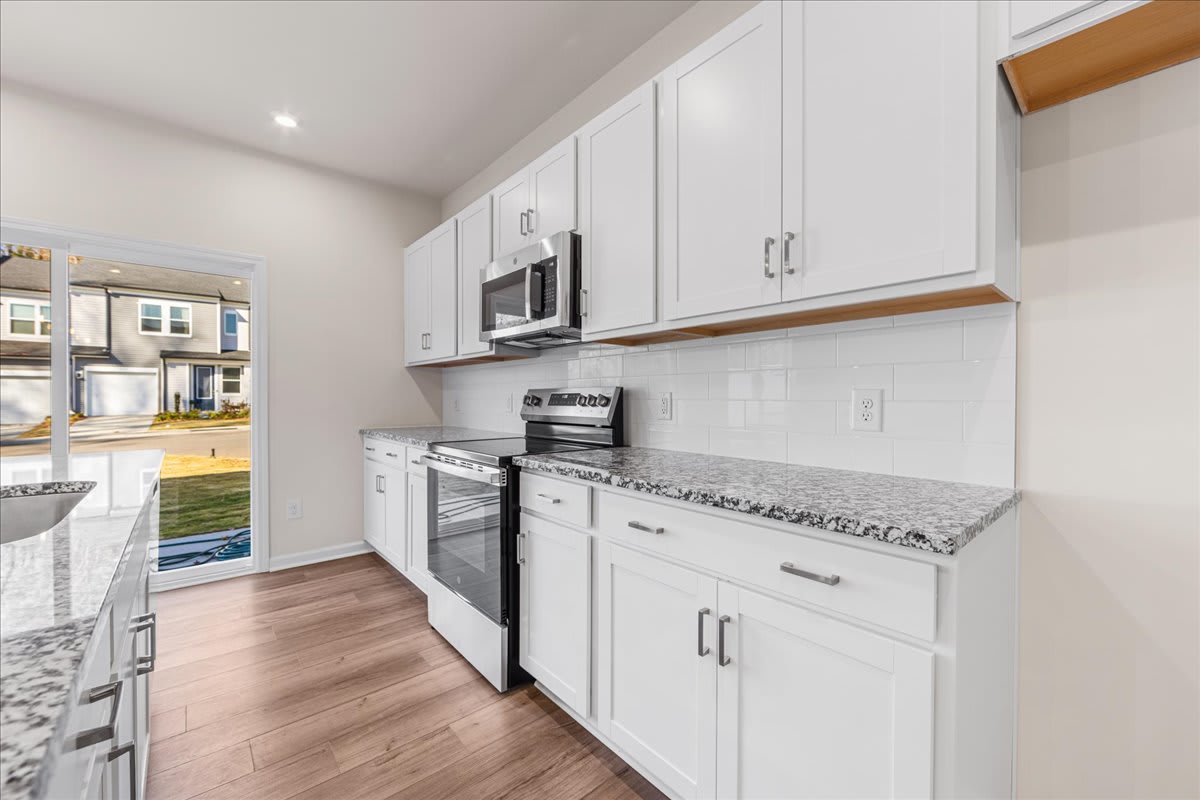 A modern, well-equipped kitchen with white cabinets, stainless steel appliances, and a granite countertop, set against a backdrop of a bright, open living space.
