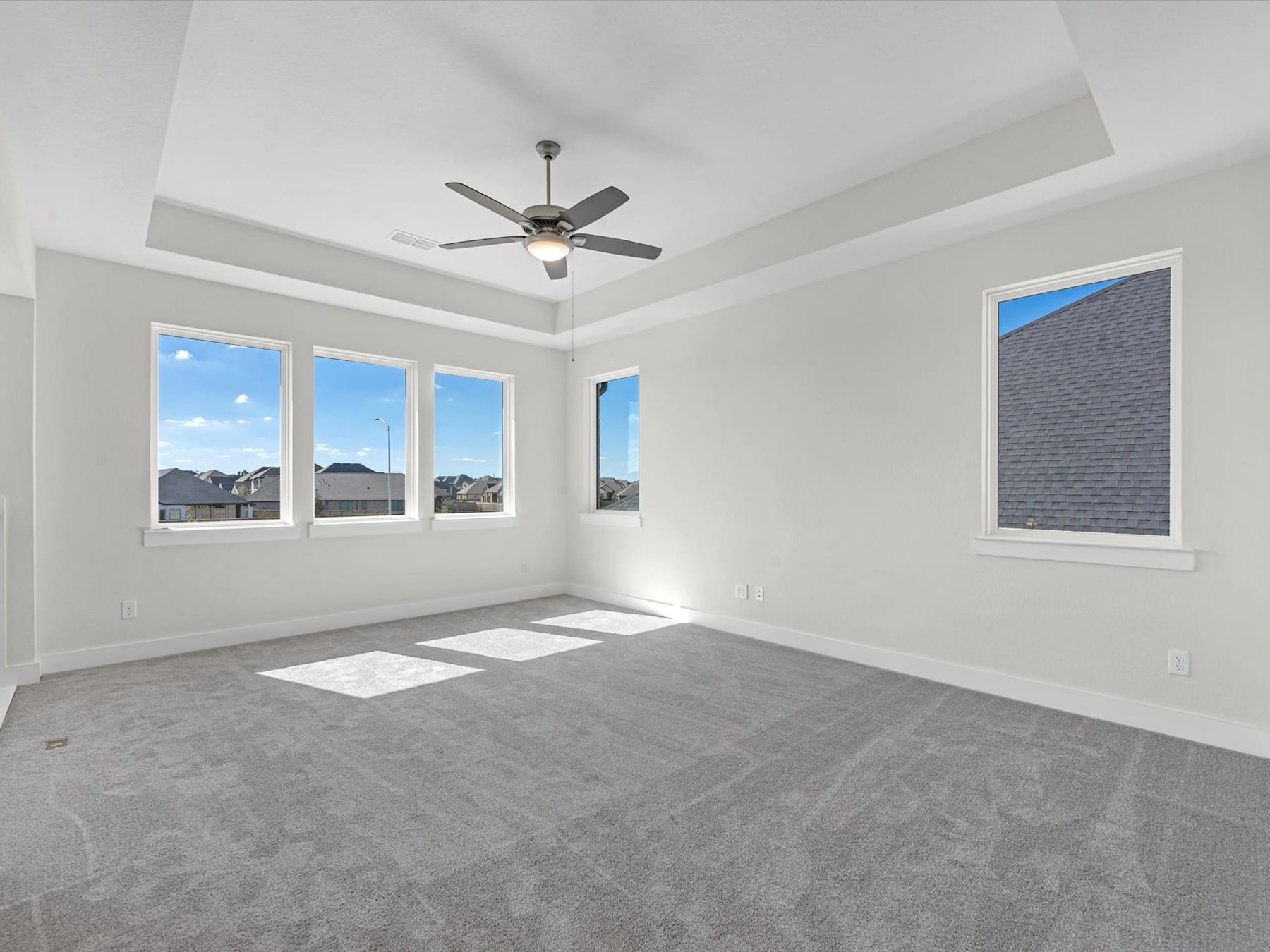 An empty, bright room with large windows, a ceiling fan, and a gray tiled floor.