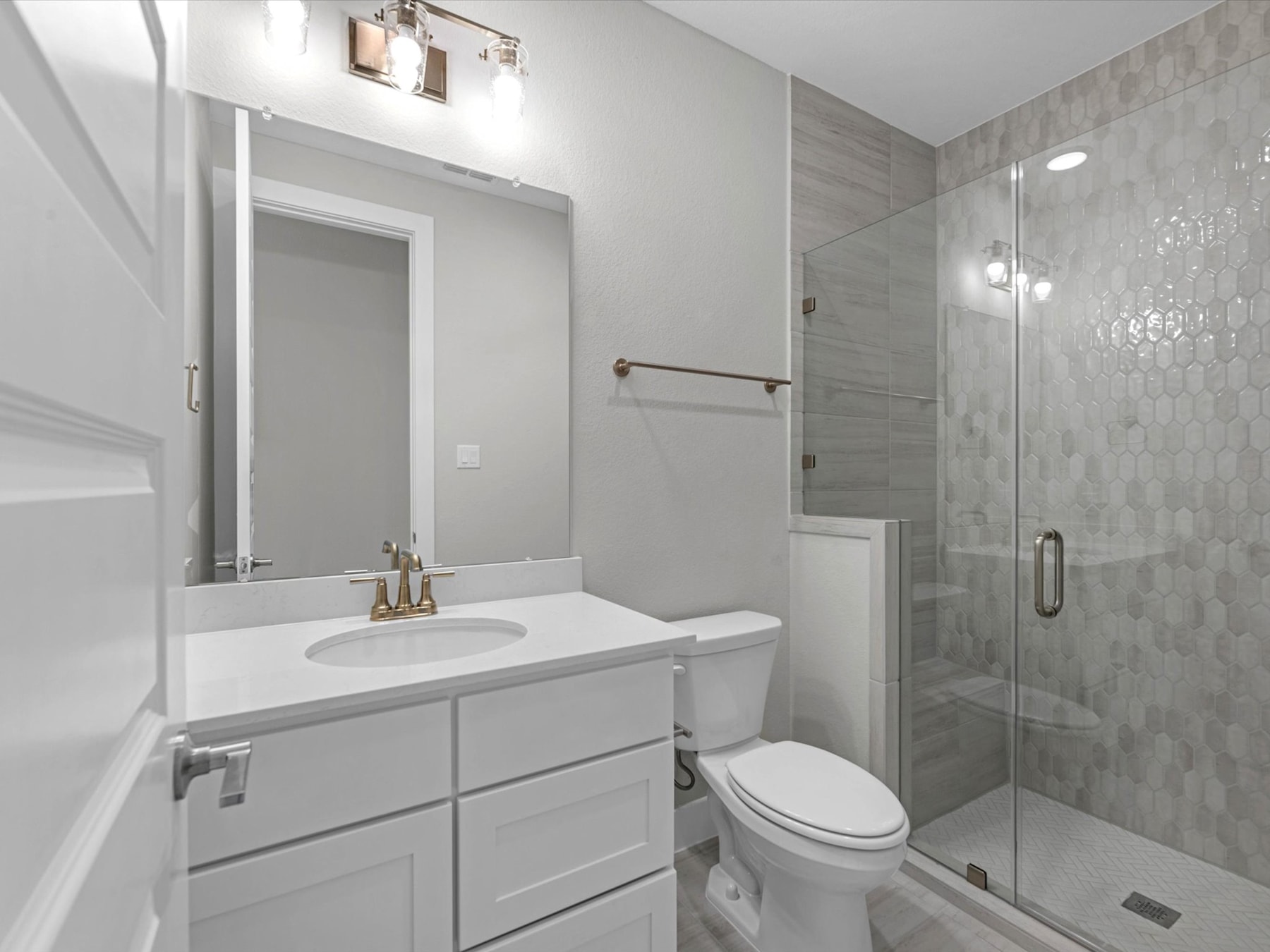 A modern, minimalist bathroom with a white vanity, a large mirror, and a glass-enclosed shower area with tiled walls.