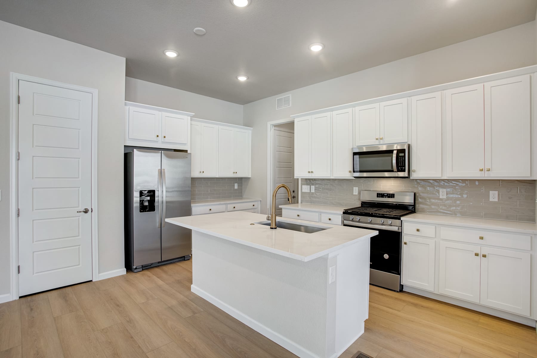 A modern, bright kitchen with white cabinets, stainless steel appliances, and a central island with a countertop.