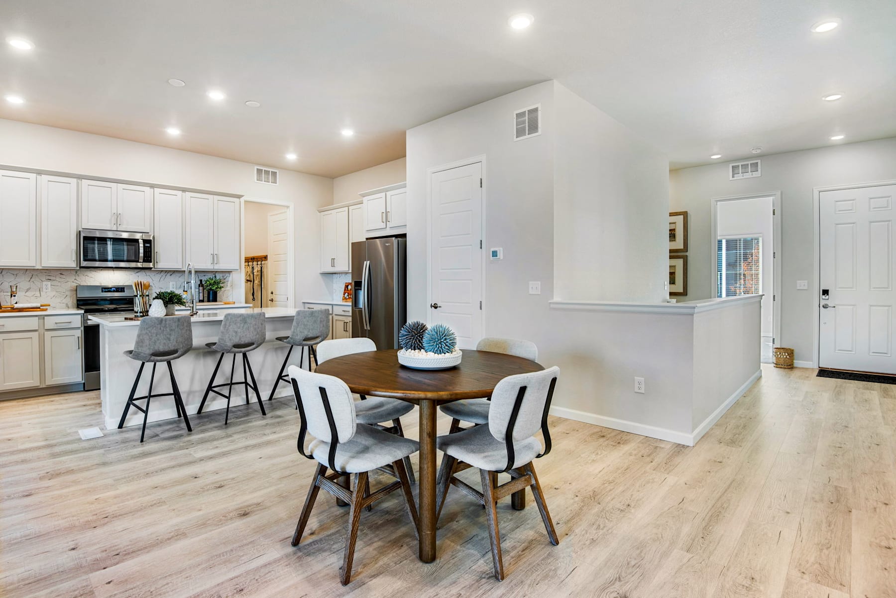 A modern, open-concept kitchen and dining area with white cabinets, stainless steel appliances, and a wooden dining table with chairs.