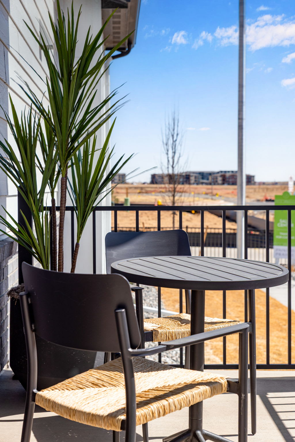 A cozy outdoor seating area with a round table and chairs, surrounded by potted plants and overlooking a scenic urban landscape in the background.