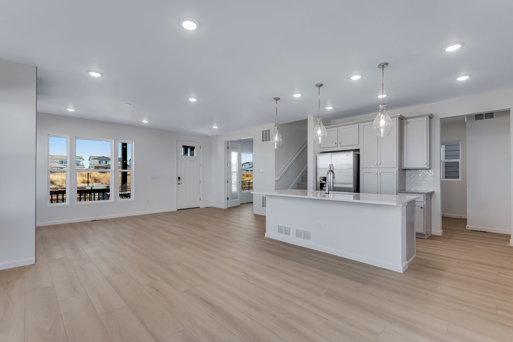 A modern, open-concept kitchen and living area with white cabinets, hardwood floors, and recessed lighting.