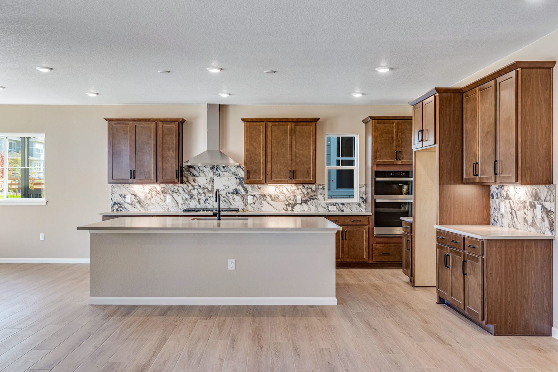 A modern and spacious kitchen with wooden cabinets, a marble countertop, and a central island, set against a bright and airy background.