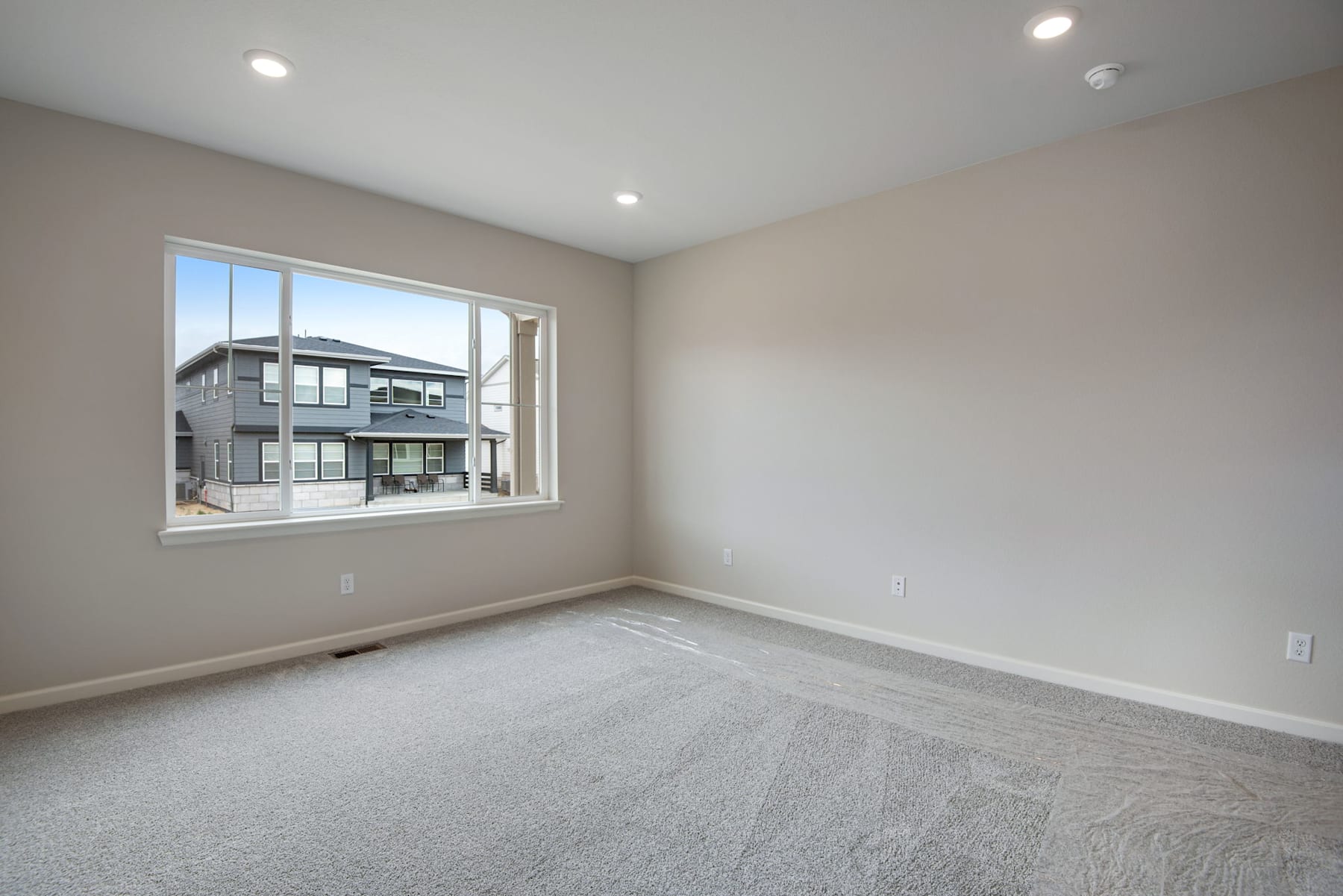 An empty room with a large window overlooking a residential neighborhood in the background.