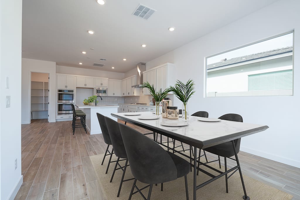 A modern, open-concept kitchen and dining area with white cabinets, a large island, and a wooden dining table surrounded by black chairs.